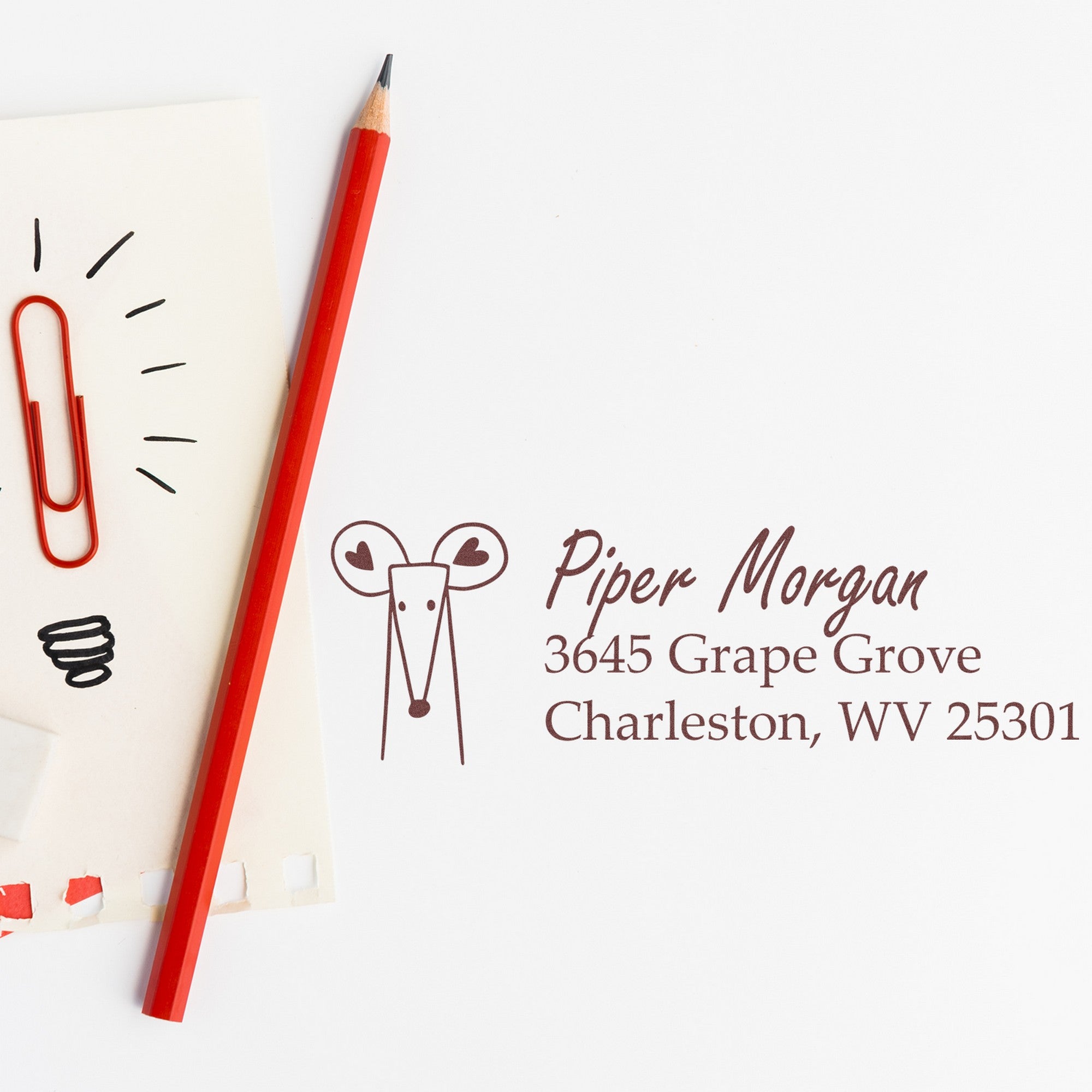 Image of a PSI Mighty Mouse Personalized Home Address Pre-Inked Stamp next to a red pencil and paper. The stamp displays "Piper Morgan, 3645 Grape Grove, Charleston, WV 25301." This Personalizable New Address Stamp is ideal for adding a custom touch.