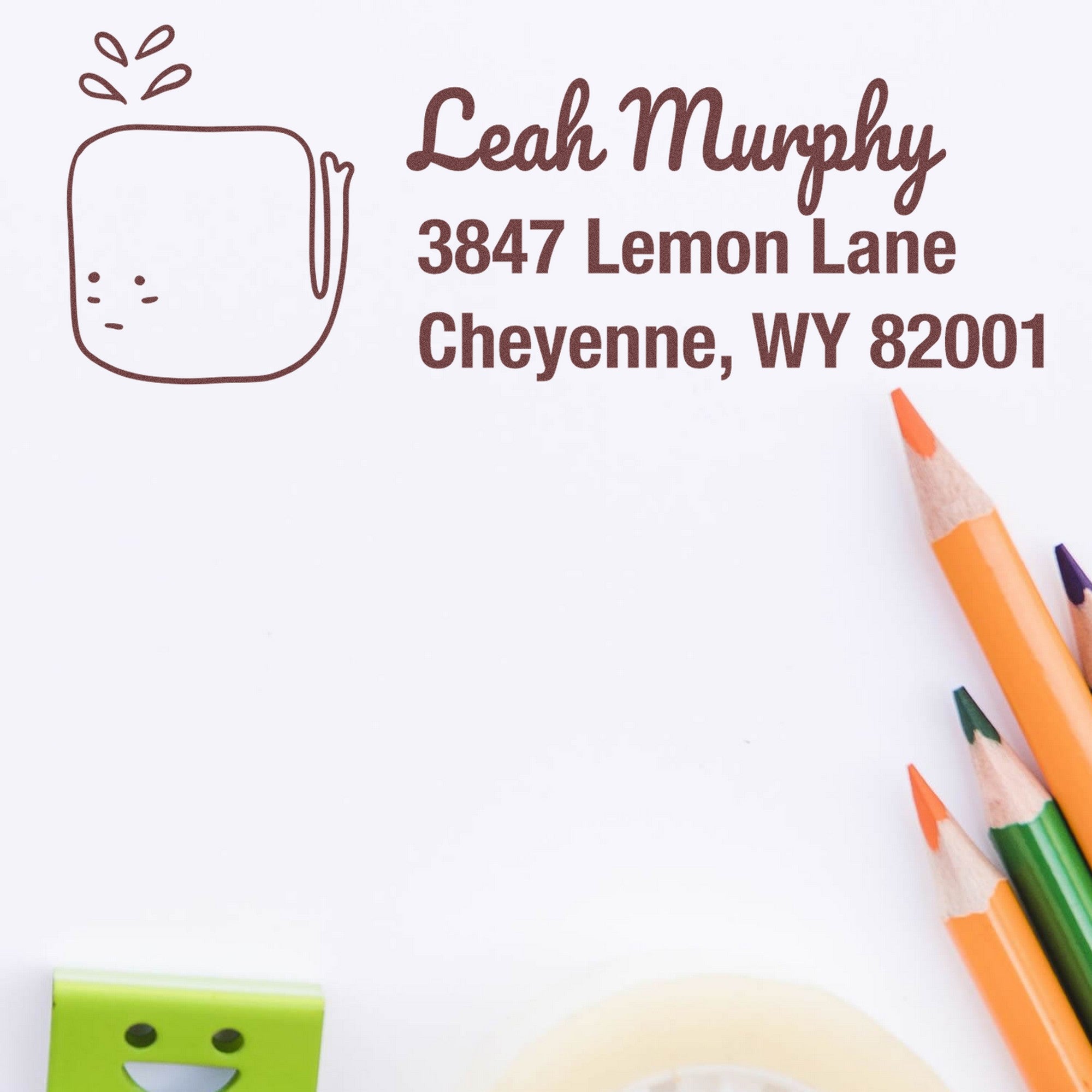 Wood Handle Joyful Whale Customize Return Address Rubber Stamp on white paper with "Leah Murphy, 3847 Lemon Lane, Cheyenne, WY 82001" in brown ink. Custom-Made New Address Stamp design with colorful pencils nearby.