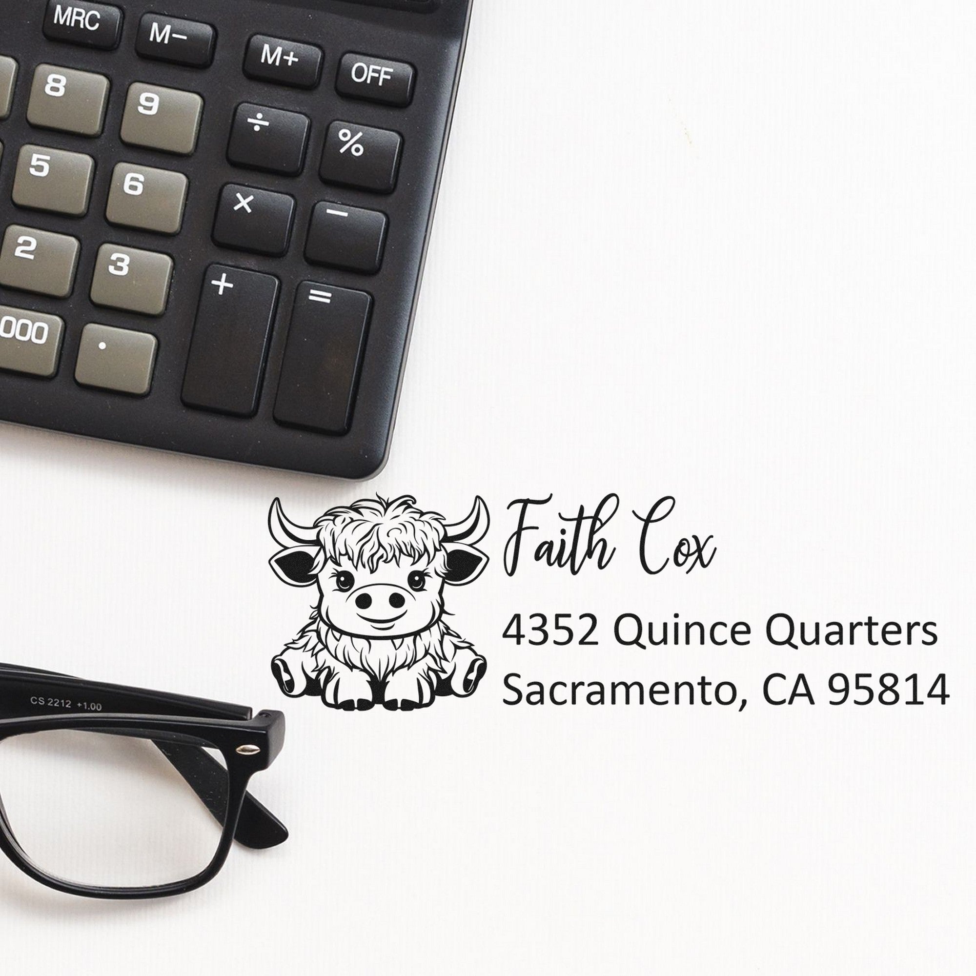 Black custom stamp and seal with cow logo and Faith Cox text on white background, beside a calculator and eyeglasses.