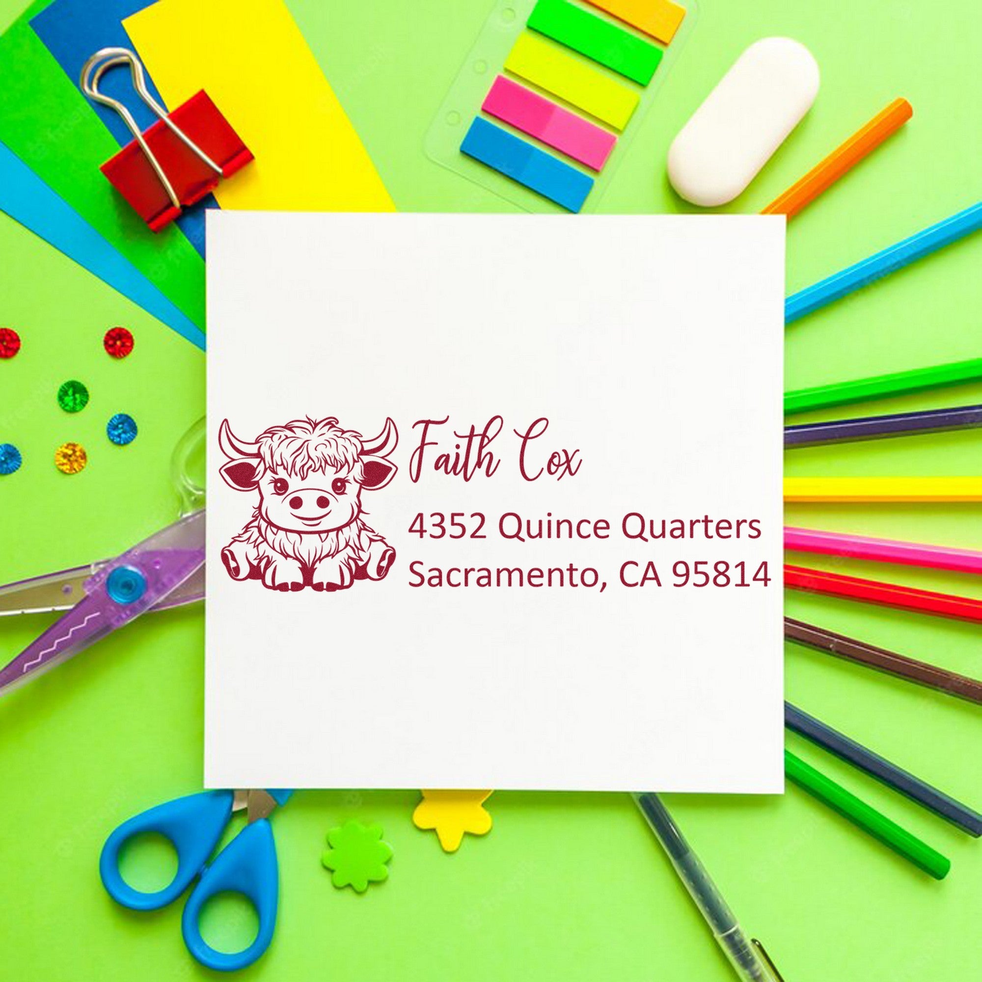 Custom maroon cow return-address stamp and seal on white envelope, with neon stationery, clips, scissors, and sticky notes.