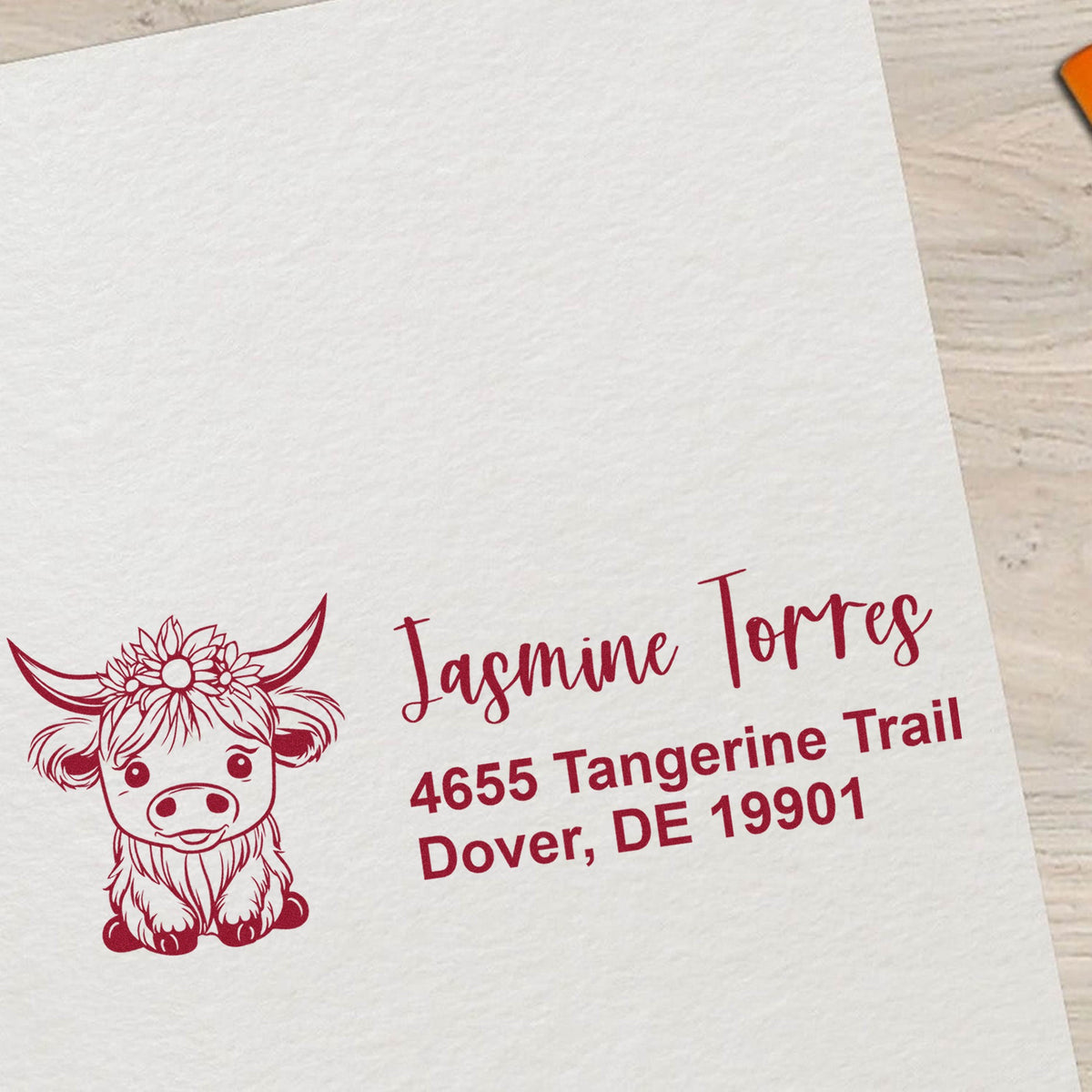 Maroon custom address stamp with cow graphic, Jasmine Torres, and Dover, DE 19901 on white paper.