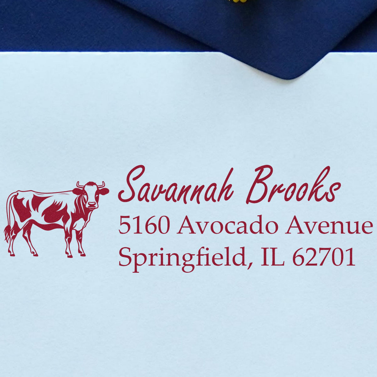 Red custom return-address stamp with cow logo for Savannah Brooks on a white envelope with navy flap.