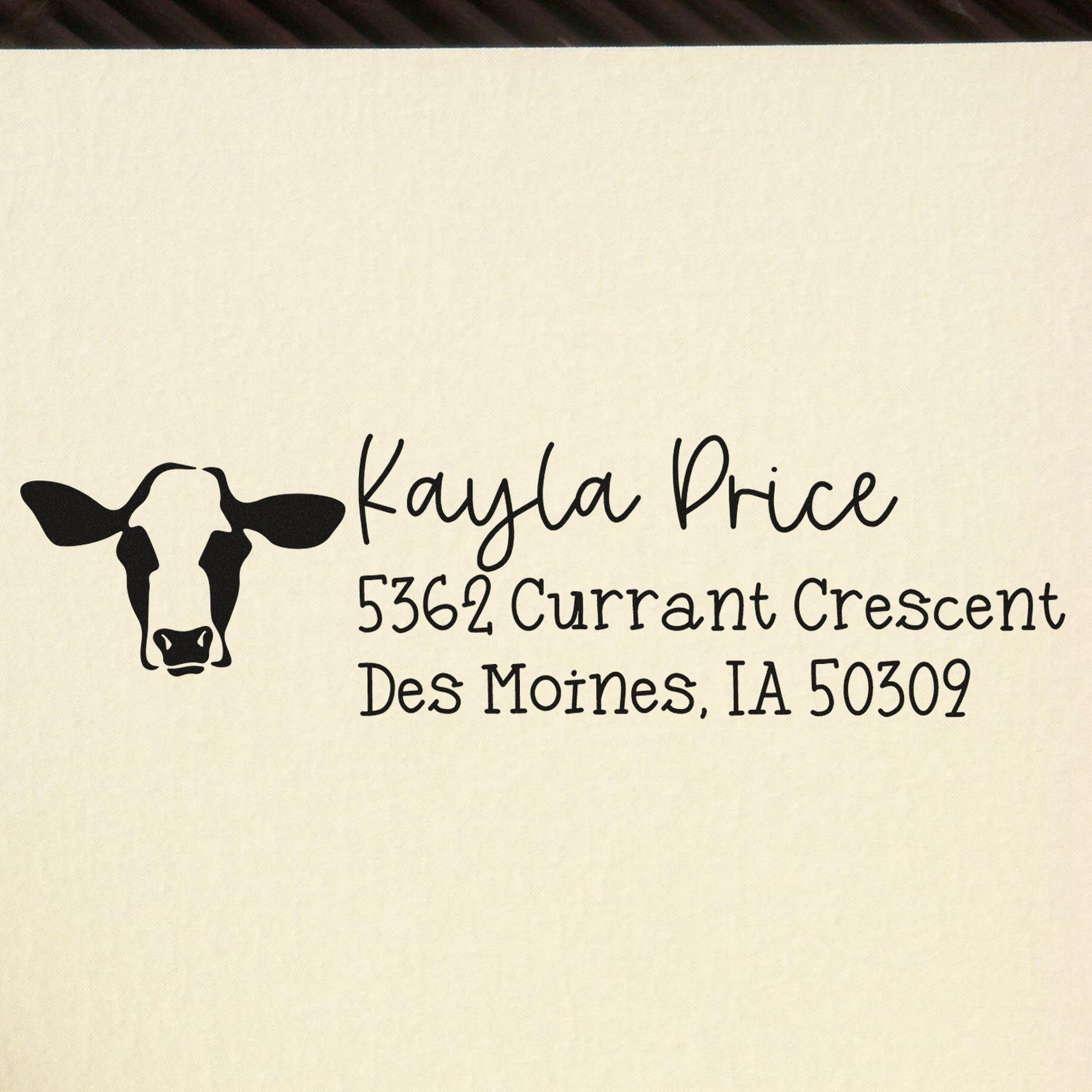 Black custom address stamp with cow logo, Kayla Price, and Des Moines address on cream background.