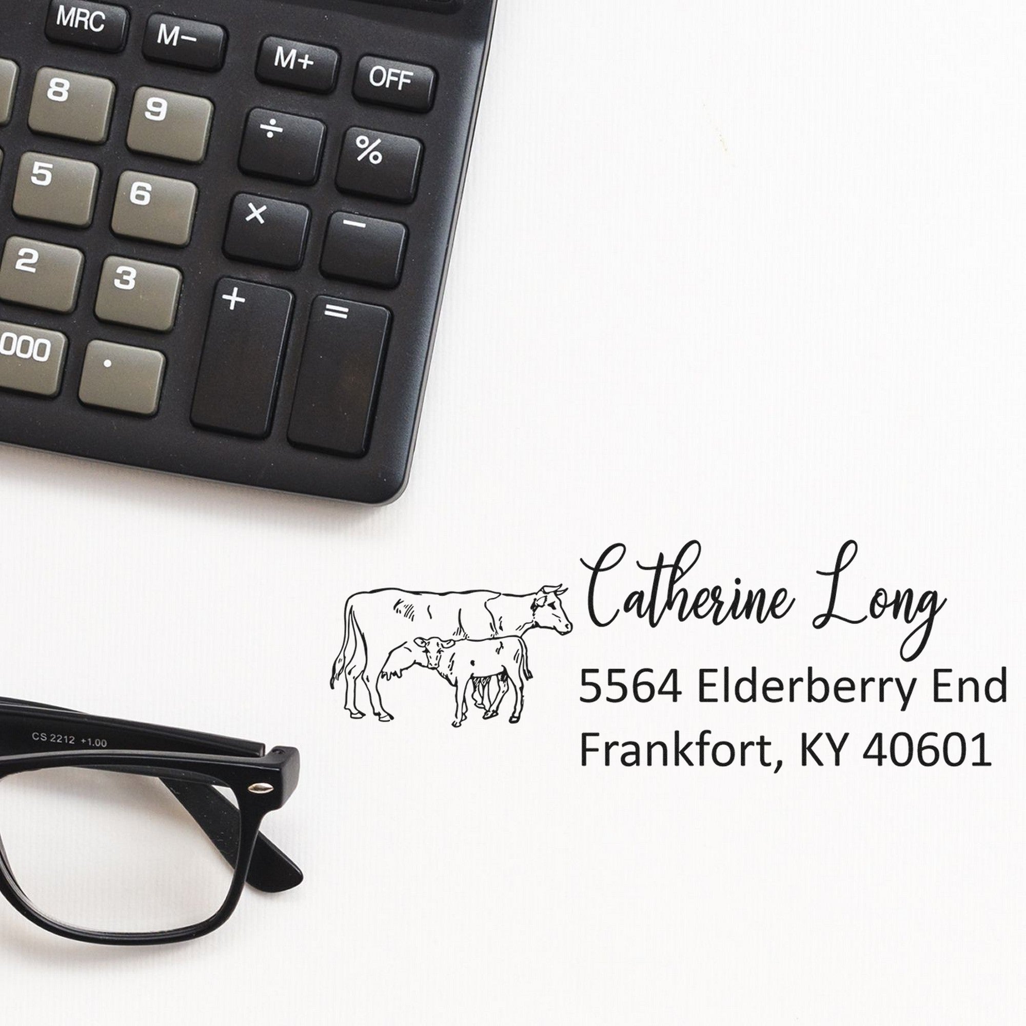 Black personalized stamp and seal with cow graphic, name and Kentucky address beside calculator and eyeglasses.