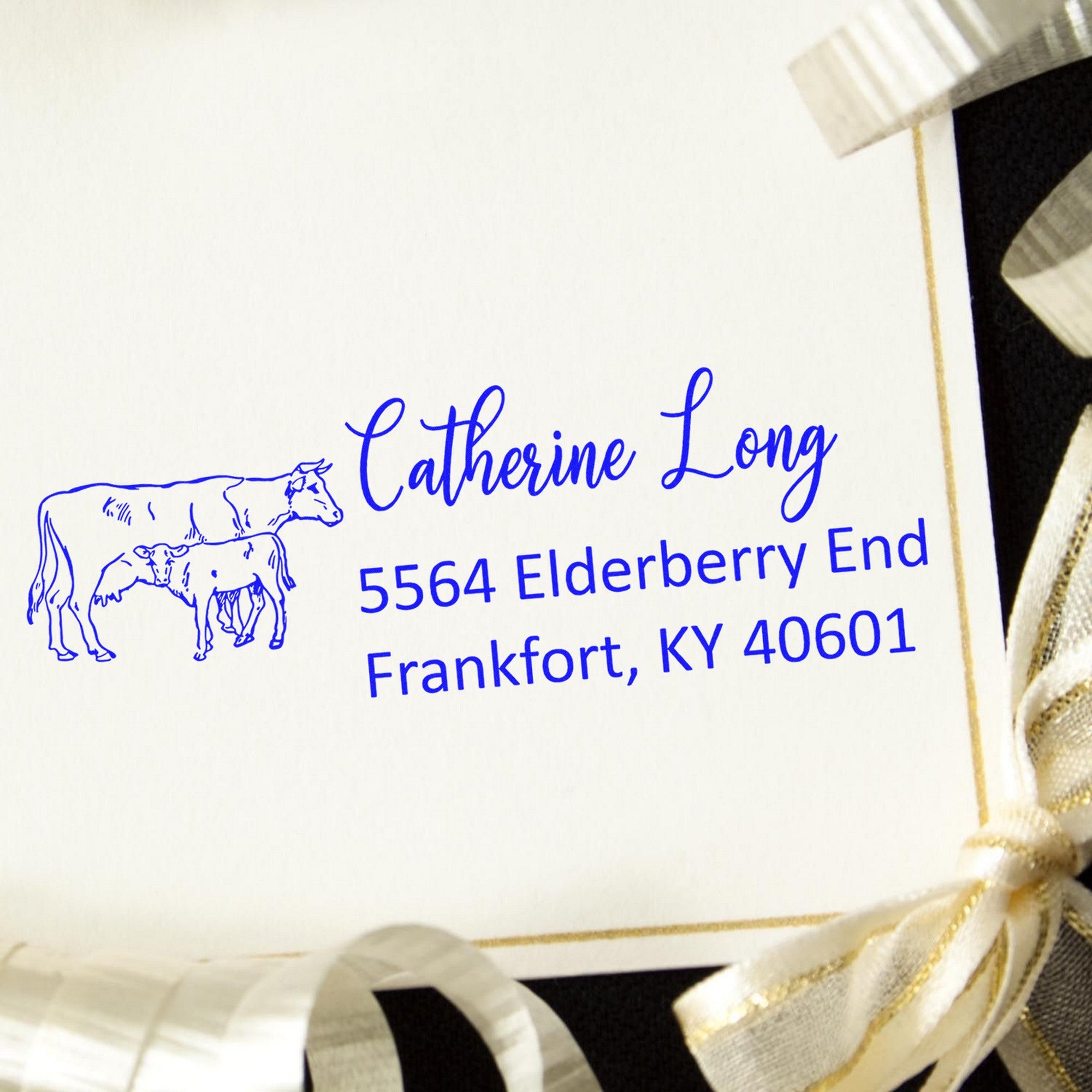 Blue personalized address stamp with cow graphic on white card, featuring Catherine Long, Frankfort KY, and gold ribbon seals.
