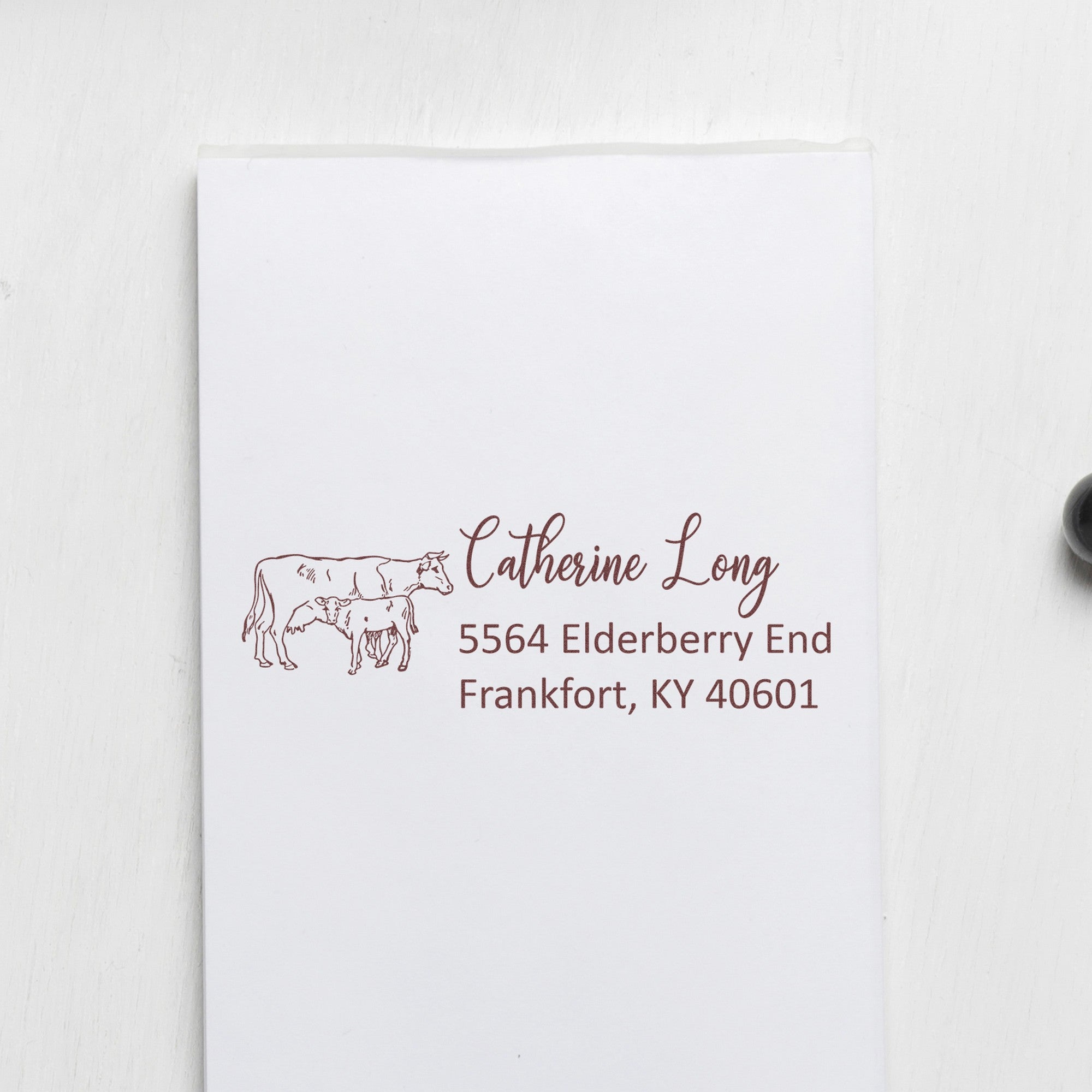 Brown custom return address stamp with cow illustration on white envelope, reading Catherine Long, Elderberry End, Frankfort KY.