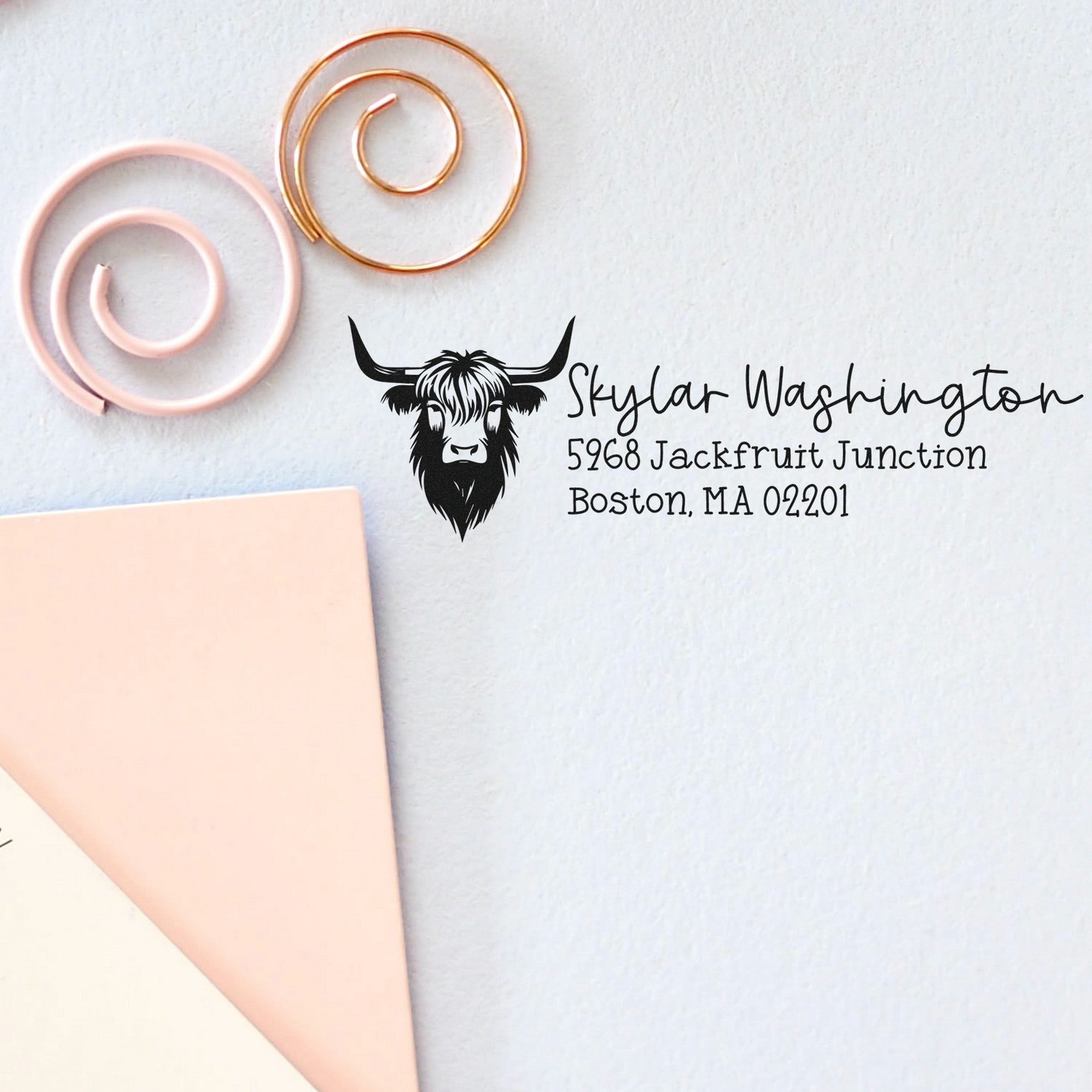 Blush pink and gold spiral stamp seals beside a black custom address stamp with cow logo on white paper.