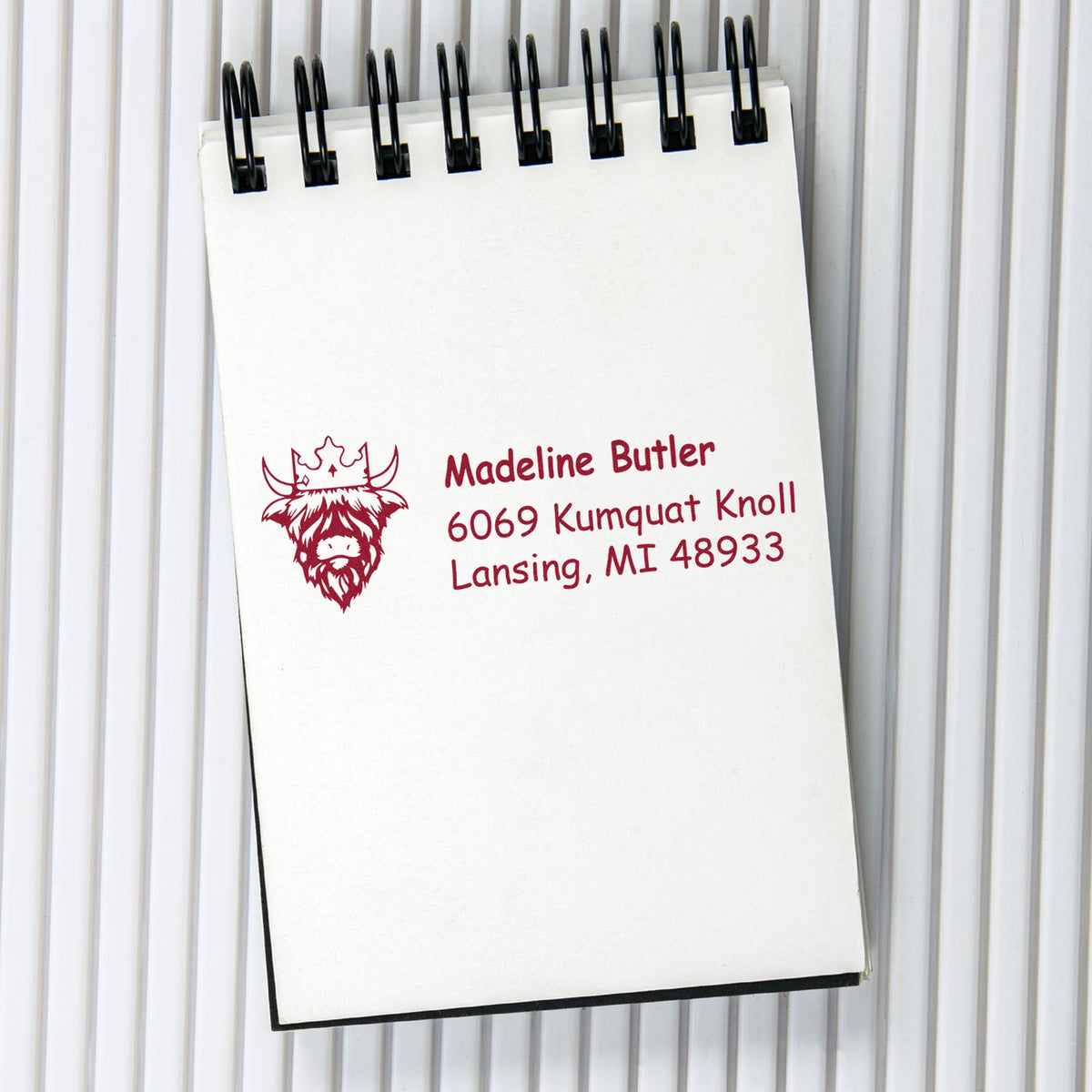 Custom burgundy address stamp and cow logo on a white spiral notepad with black binding.
