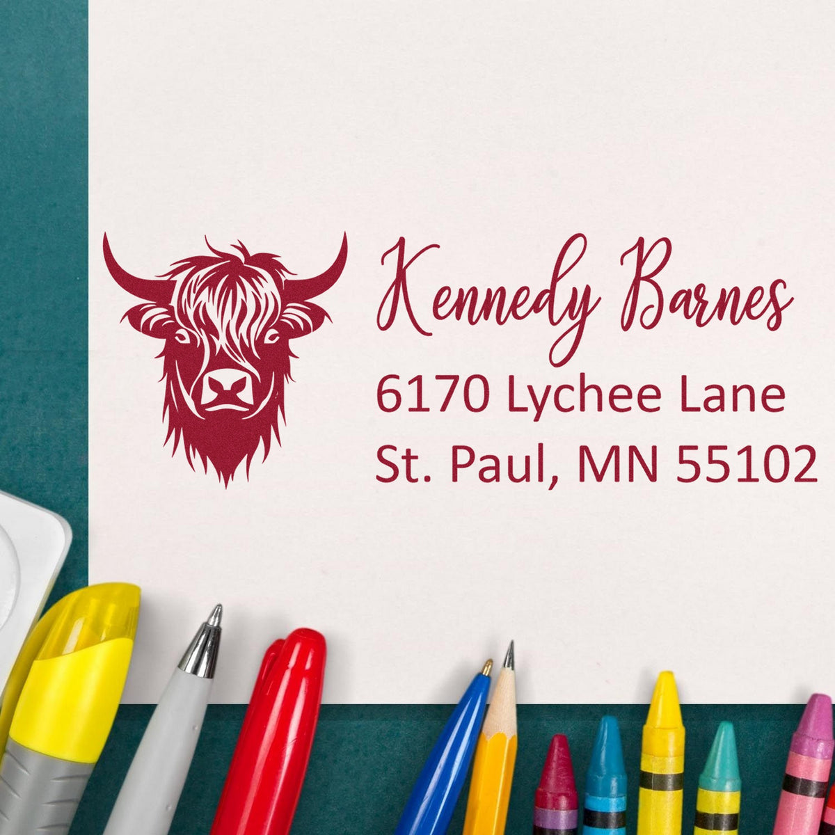 Maroon custom stamp/seal with cow head logo, Kennedy Barnes, St. Paul address on white paper, surrounded by colorful pens.