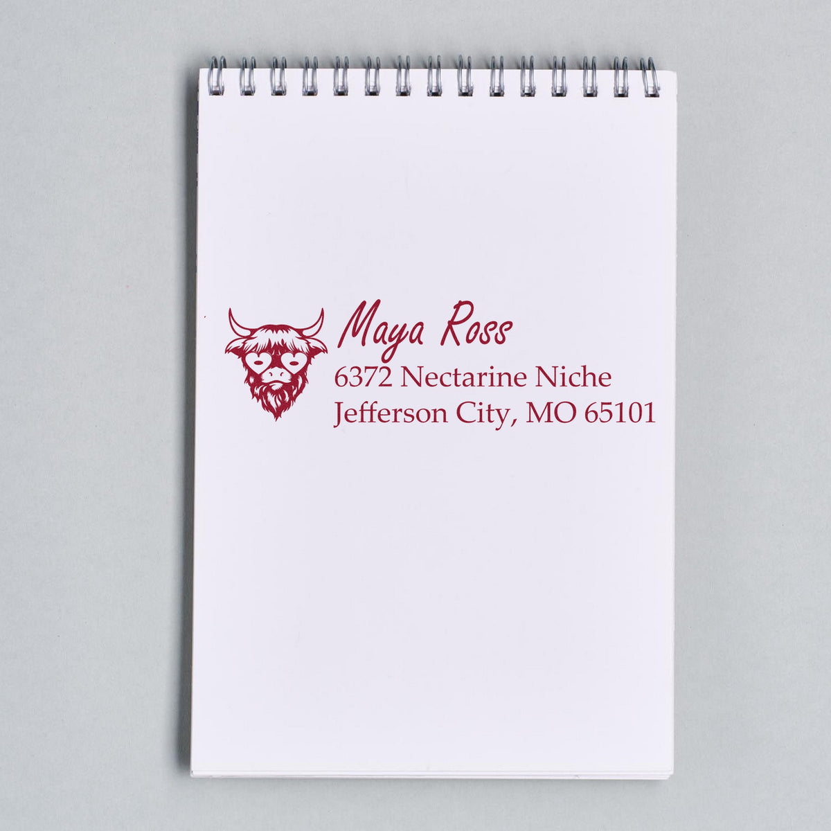 Maroon custom address stamp with llama seal on white spiral notepad, showing Maya Ross and Jefferson City, MO address