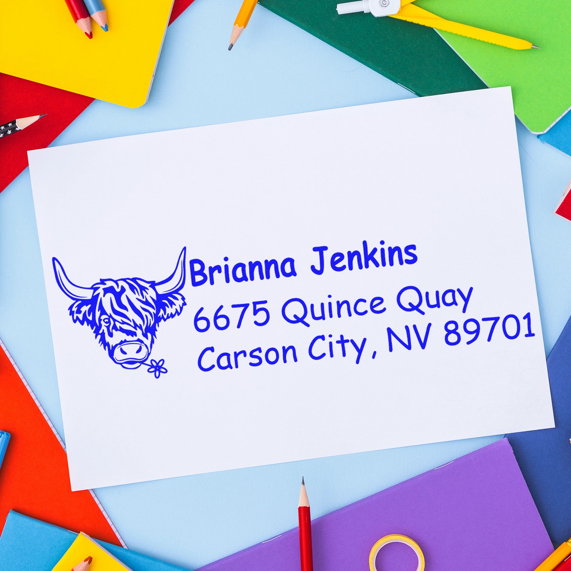 Blue custom return-address stamp with longhorn seal on white envelope, surrounded by colorful pencils and notebooks