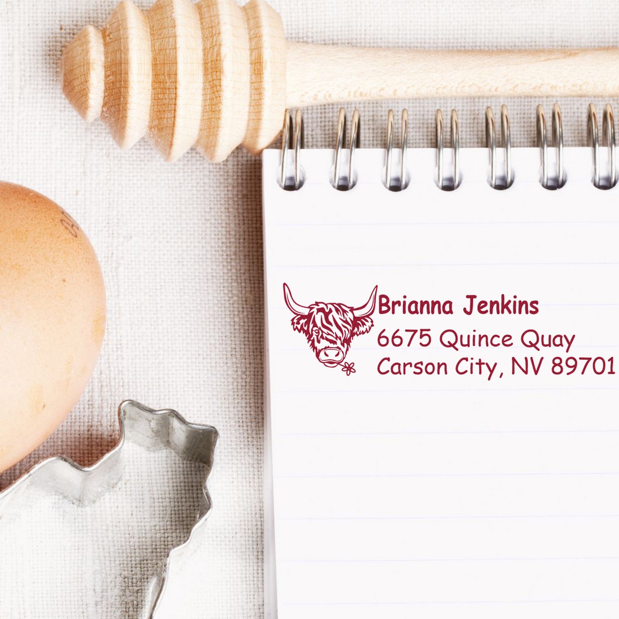 Maroon custom stamp and seal with cow logo and address on a spiral notepad beside baking tools