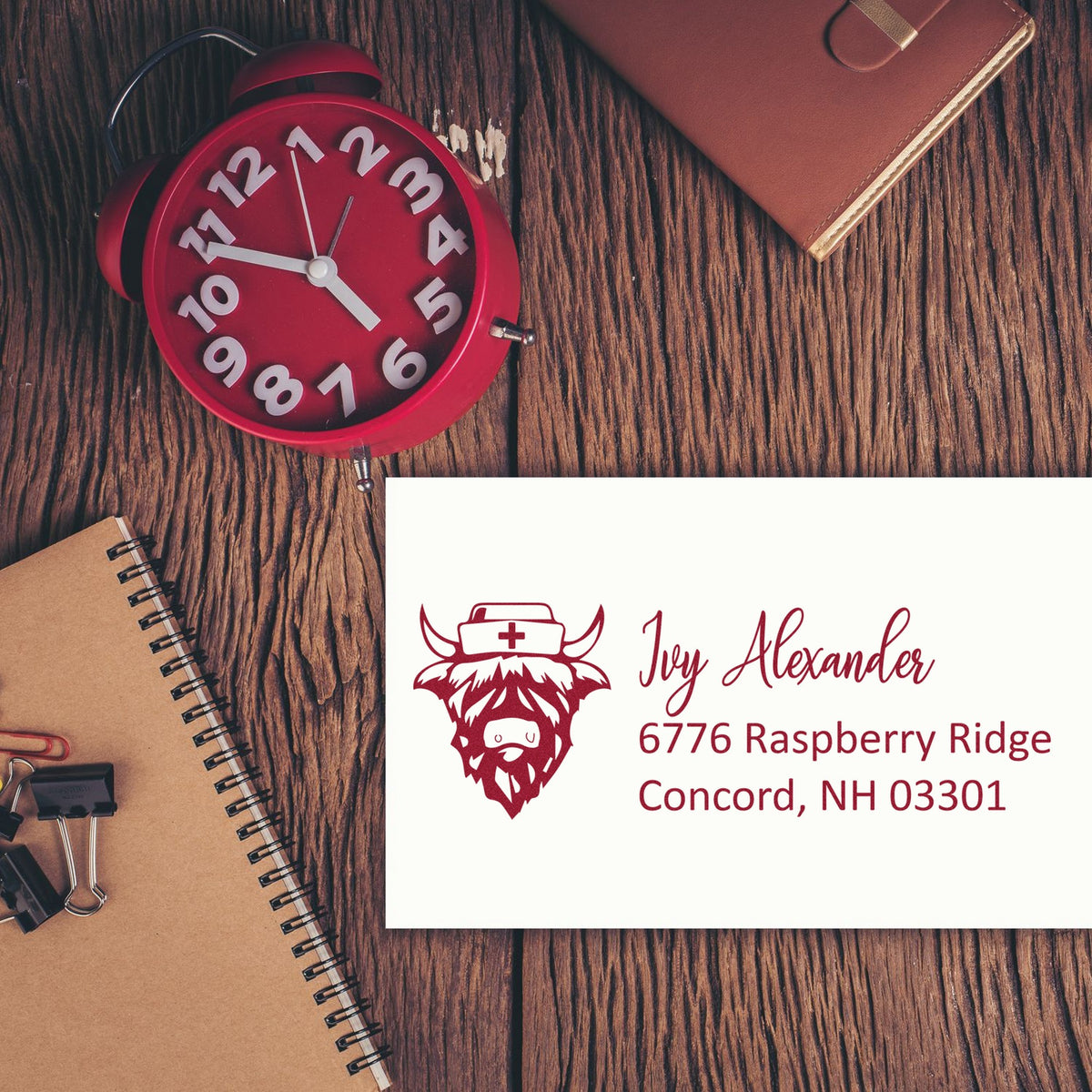Red custom stamp and seal products on a wood desk, with maroon logo, name, and address beside a red vintage clock.