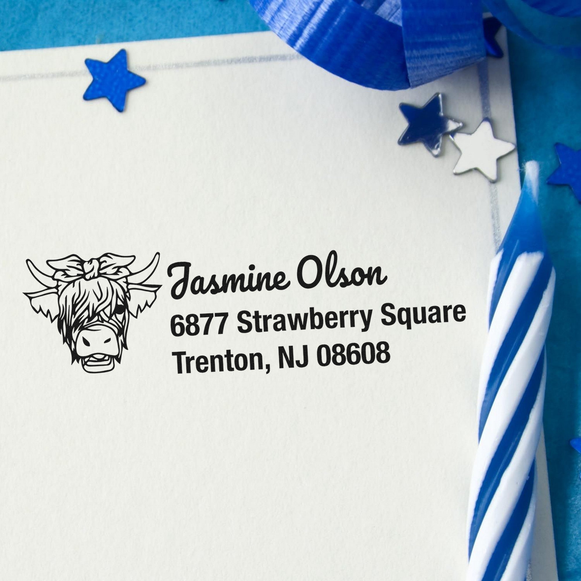 White envelope with black custom address stamp, cow logo, and blue star seals with striped blue ribbon accents
