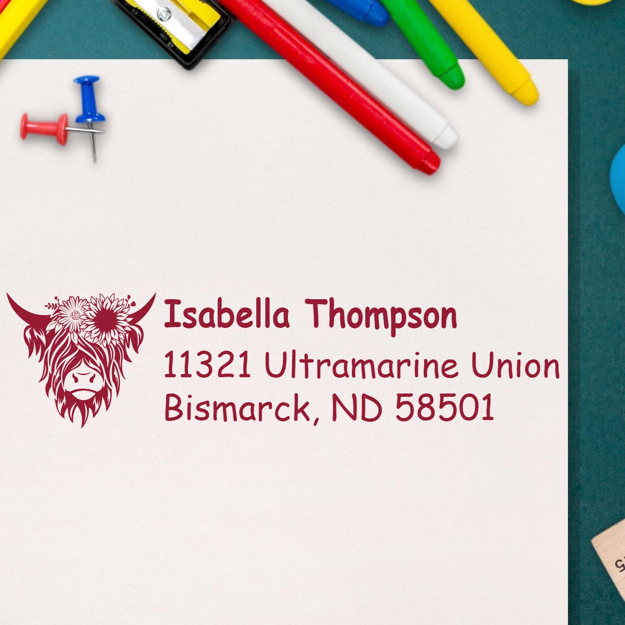 Burgundy personalized address stamp and seal with cow logo, Isabella Thompson name, and Bismarck, ND address beside colorful pens.