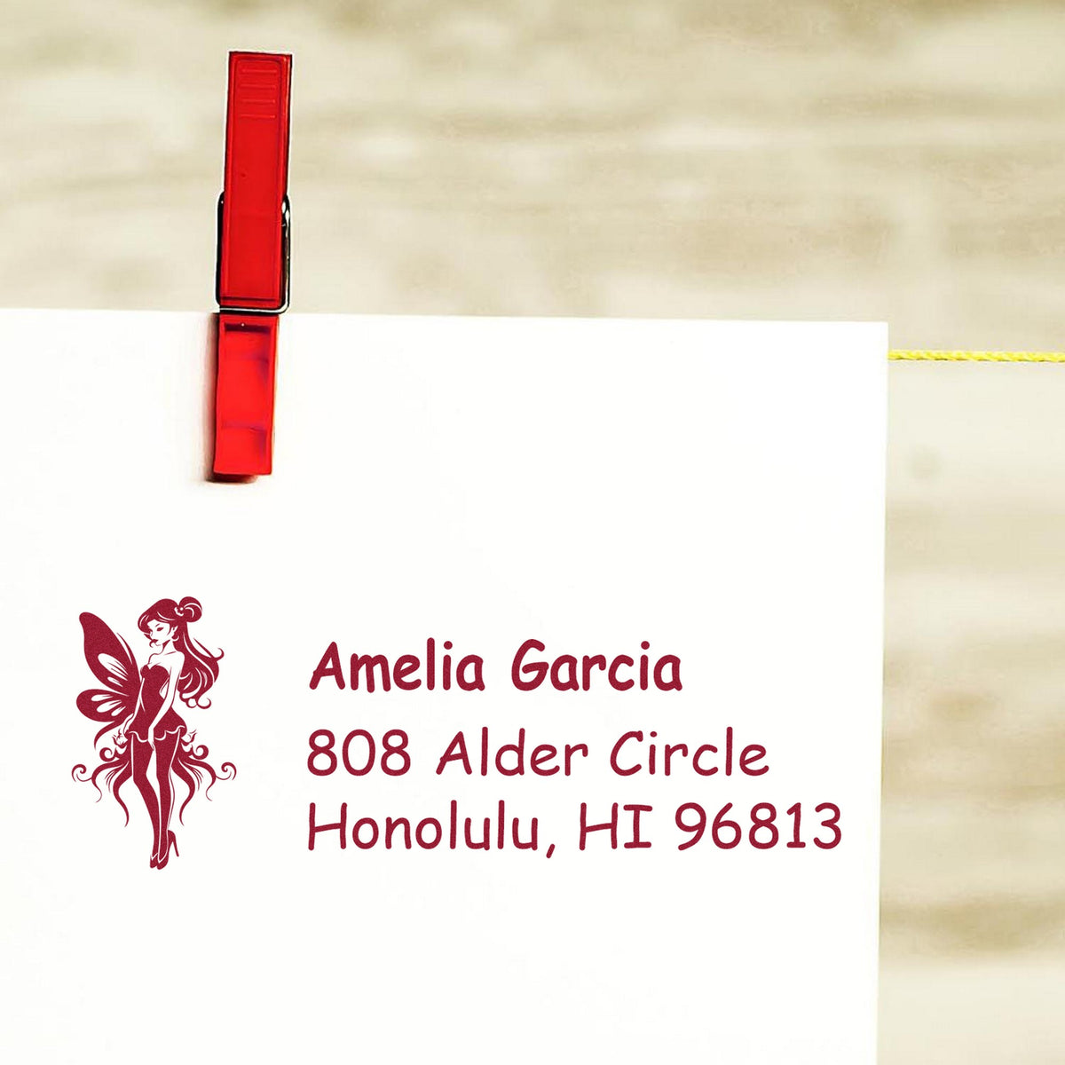 Custom burgundy stamp and seal card clipped with a red clothespin, featuring a fairy logo and Amelia Garcia address.