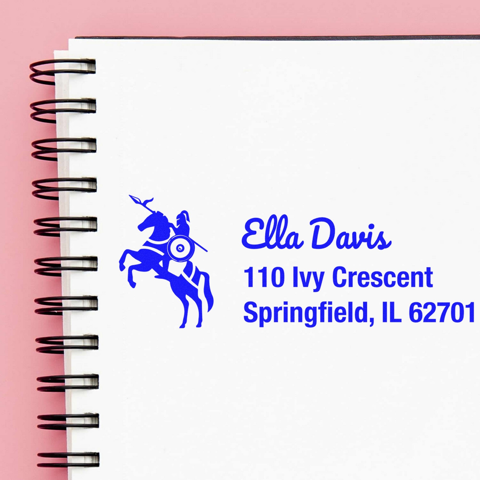 Custom blue horse stamp seal on white spiral notebook, pink background, black coils, with Ella Davis address and Springfield, IL 62701