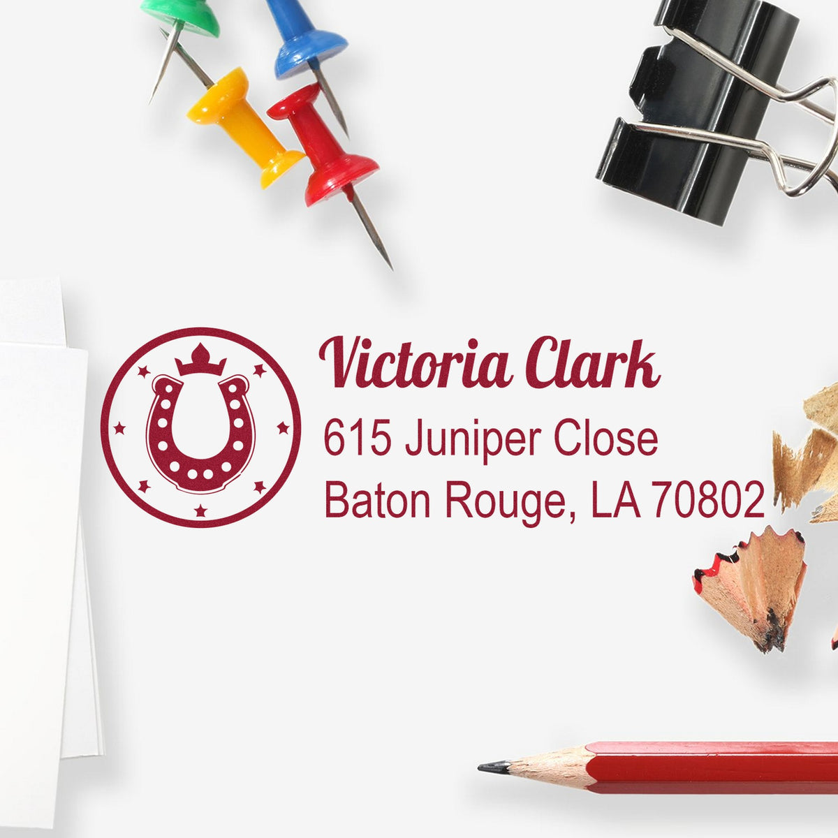 Custom burgundy horseshoe address stamp and seal for Victoria Clark, with colorful push pins, pencils, and a binder clip.