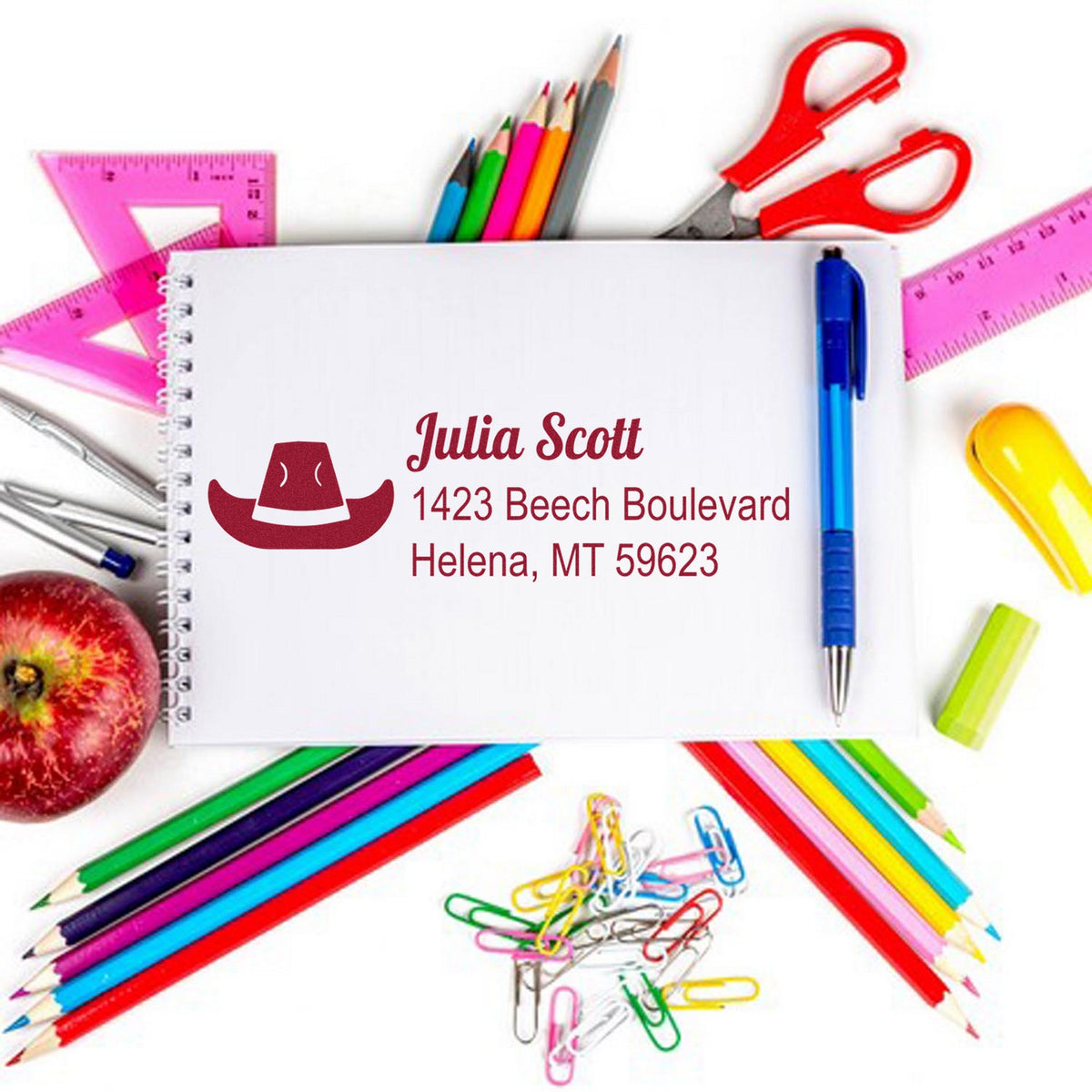 Personalized red stamp and seal with name and address, surrounded by colorful pencils, rulers, and scissors.