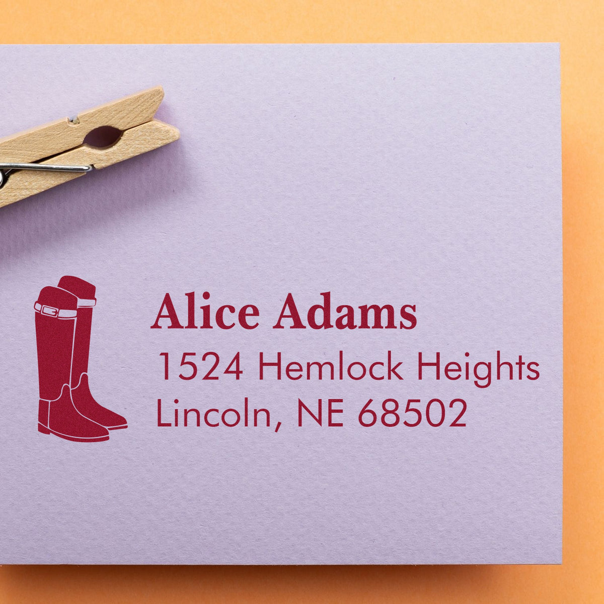 Lavender envelope with red custom address stamp and boot seal, clipped by a wooden clothespin on orange background.