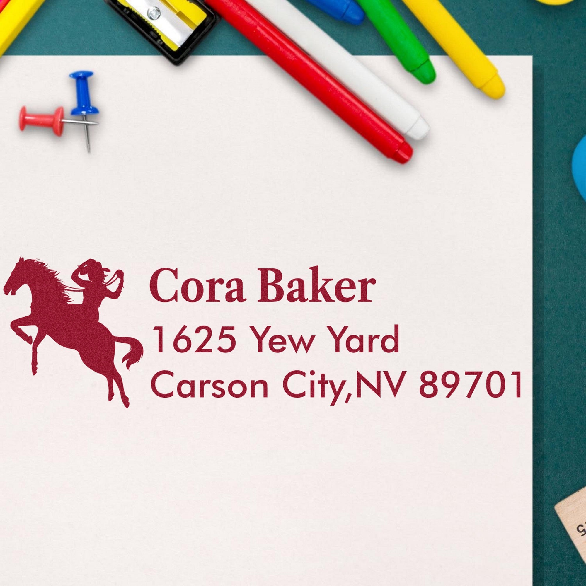 Custom burgundy horse address stamp and seal on white paper, with colorful pens and push pins on a teal background