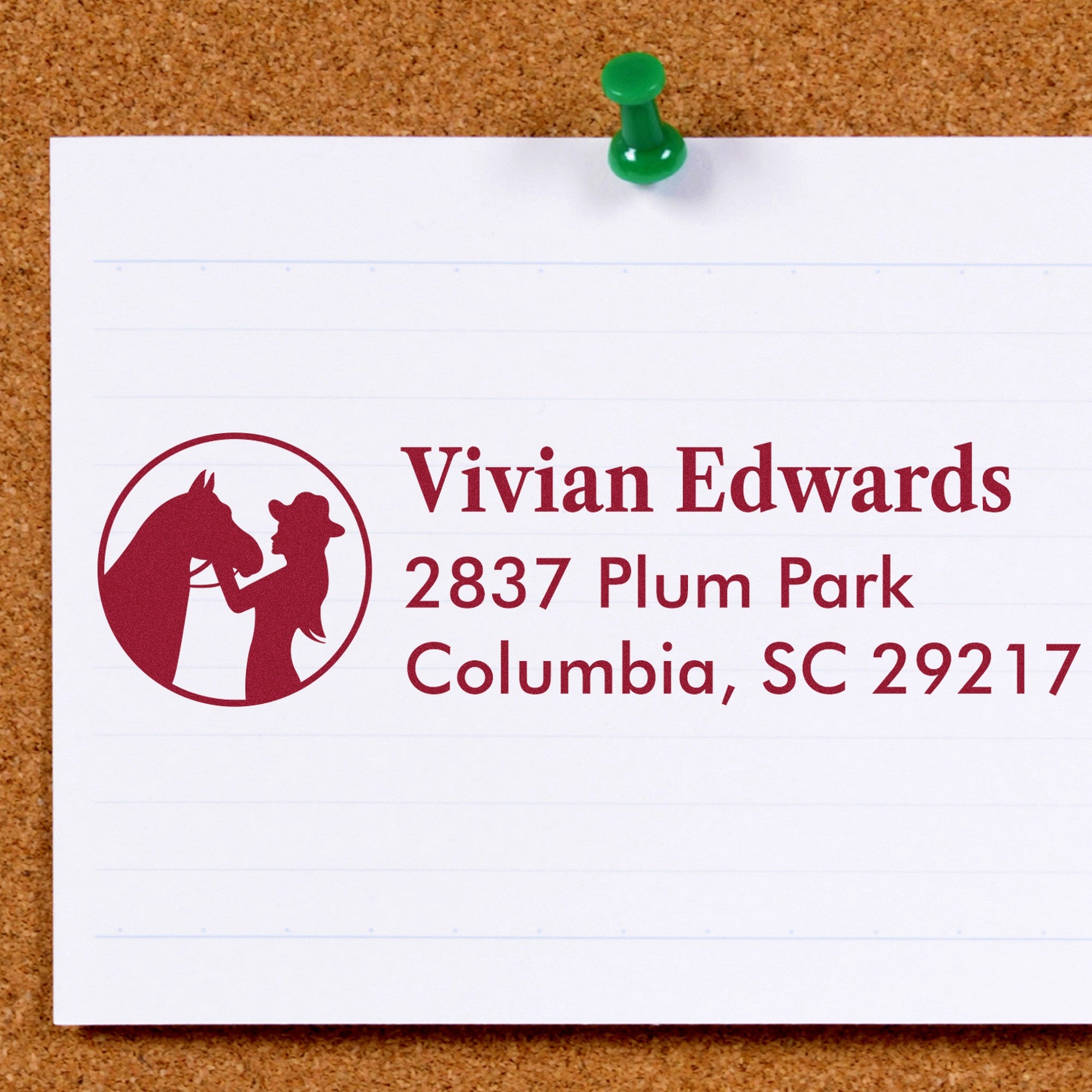 Maroon custom stamp seal with horse and rider logo, pinned to corkboard with a green pushpin on white paper.