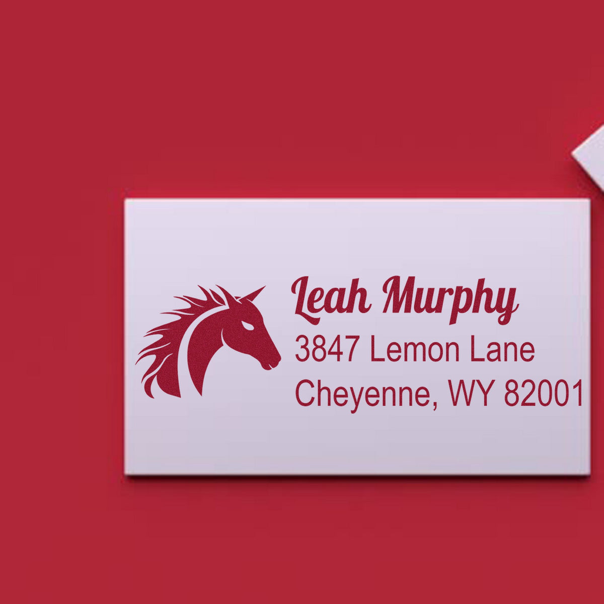 Burgundy custom address stamp and seal with horse logo, Leah Murphy, Cheyenne WY, on a white card against a red background.