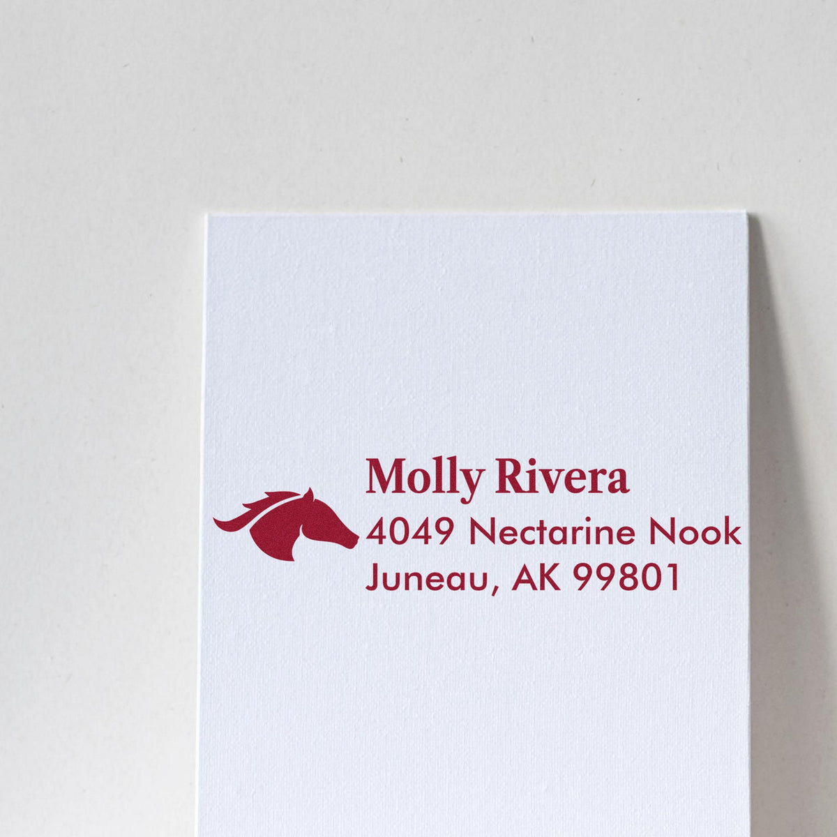 Burgundy custom address stamp with horse logo and Molly Rivera address on white textured paper.