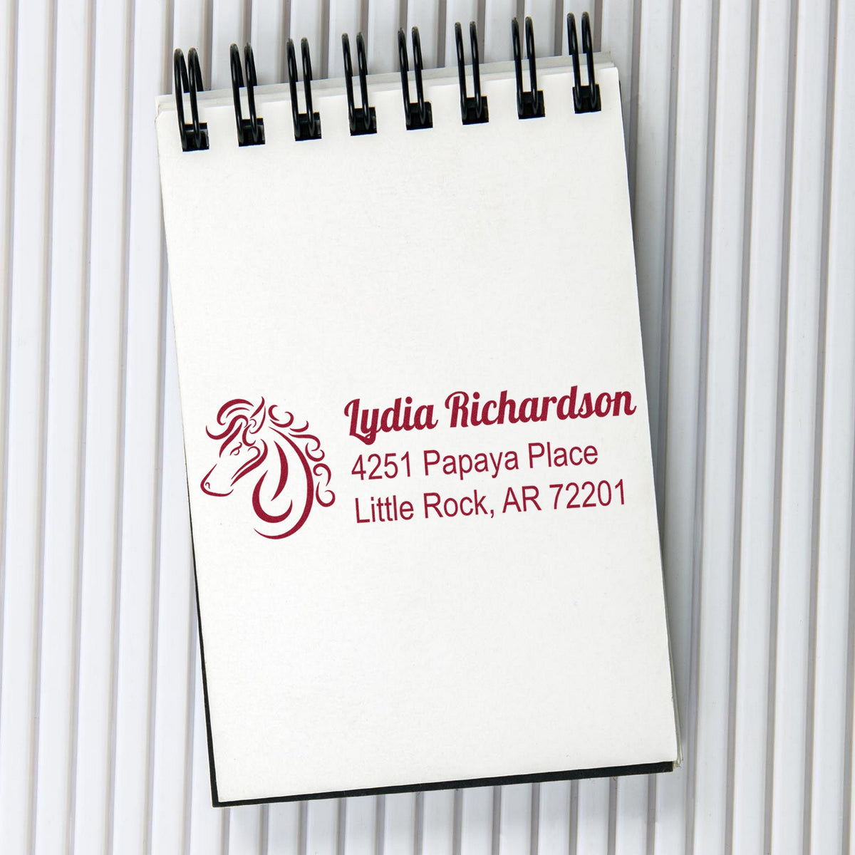 White spiral notepad with maroon custom stamp and seal imprint, horse logo, name, and address on a white background.