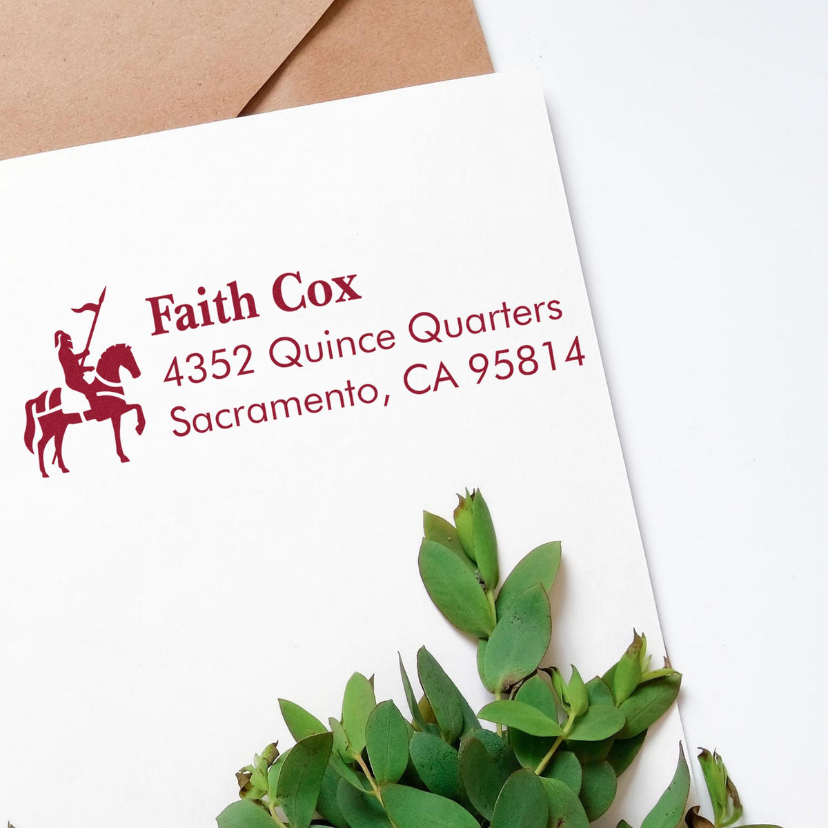 Maroon address stamp and seal with horse rider on white envelope, Faith Cox, Sacramento CA, beside kraft paper and green leaves
