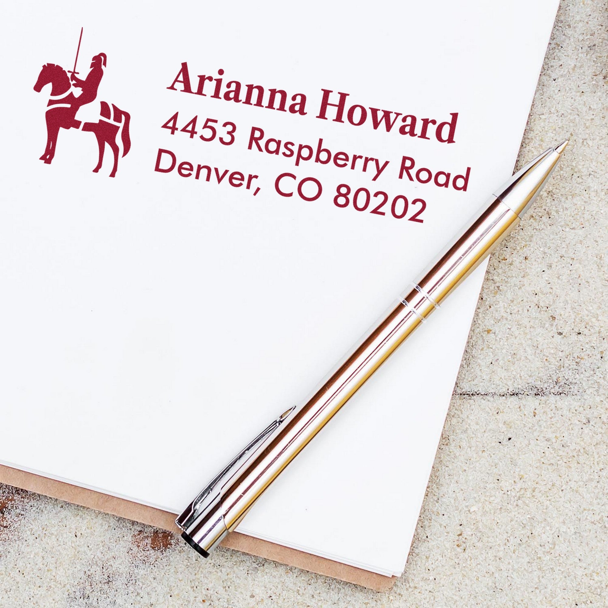 Burgundy custom return address stamp and seal with horse rider, on white stationery beside a gold-and-silver pen.