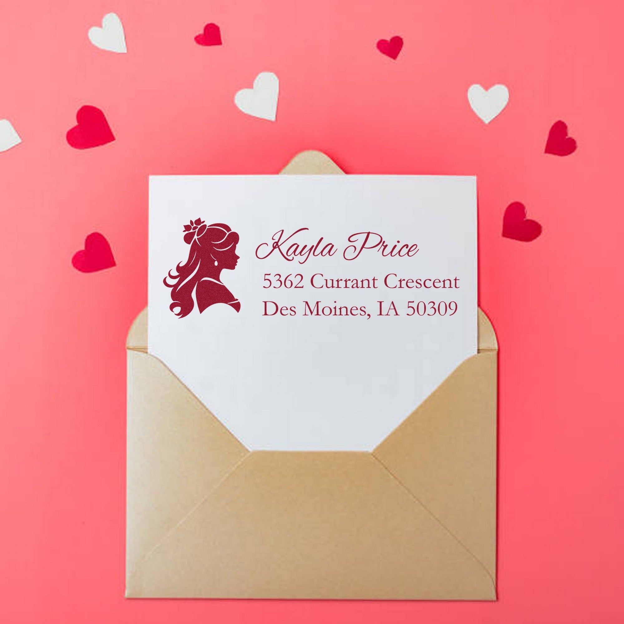 Custom burgundy address stamp and seal on white card in tan envelope, against a pink background with heart confetti.