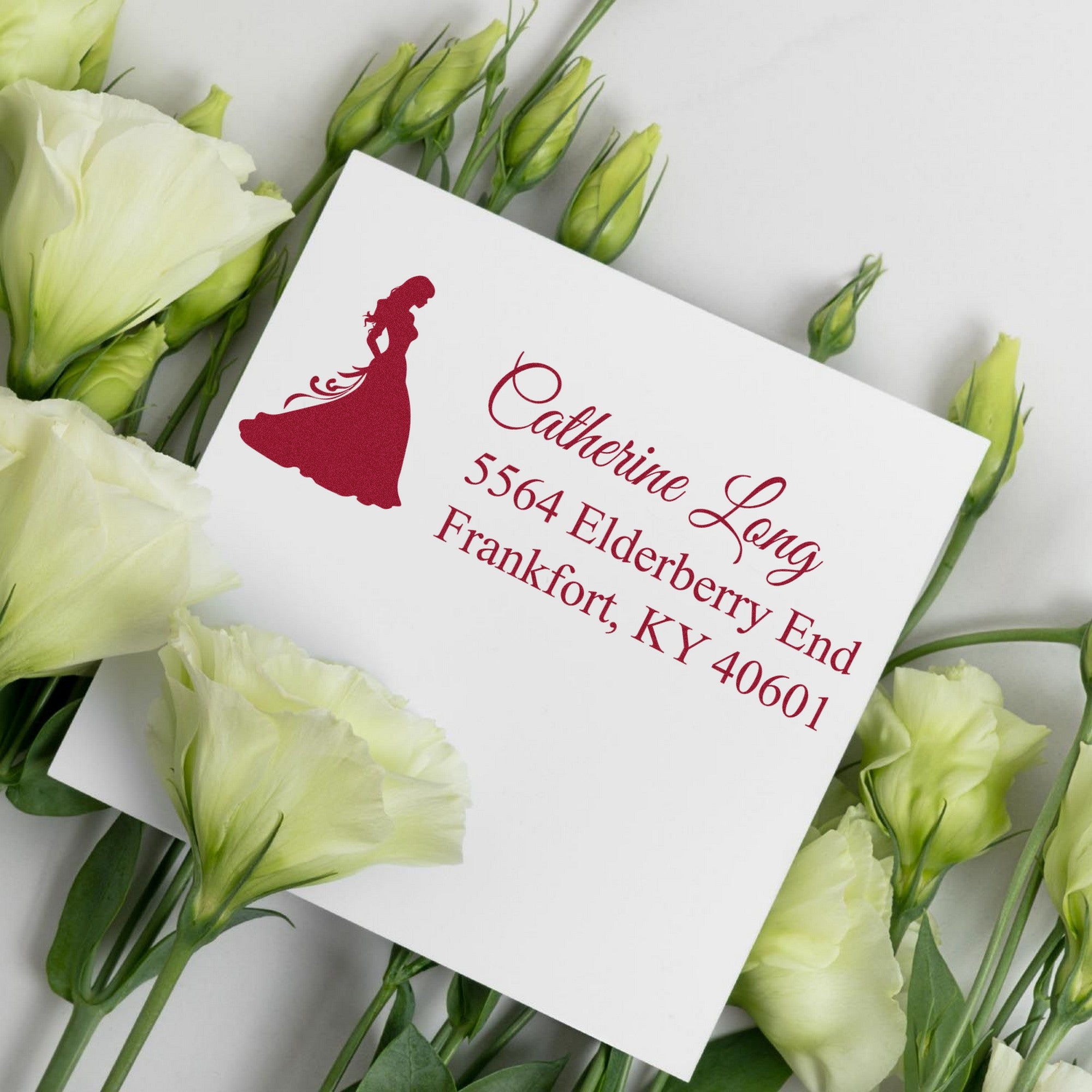 White custom wedding stamp and seal card with burgundy bride silhouette and script, surrounded by pale green and cream flowers.