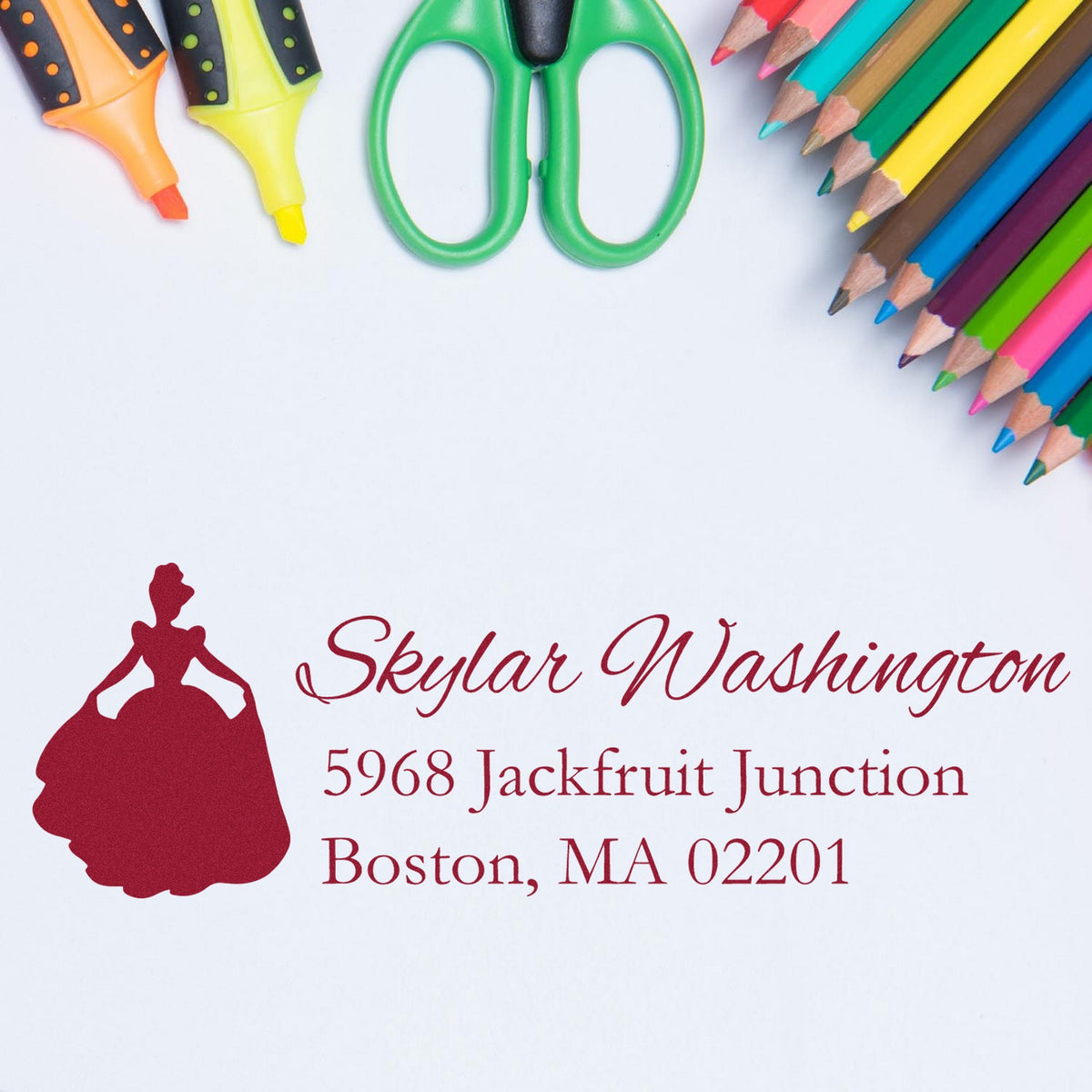 Red custom seal stamp with Skylar Washington address on white paper, beside colorful pencils, markers, and green scissors.