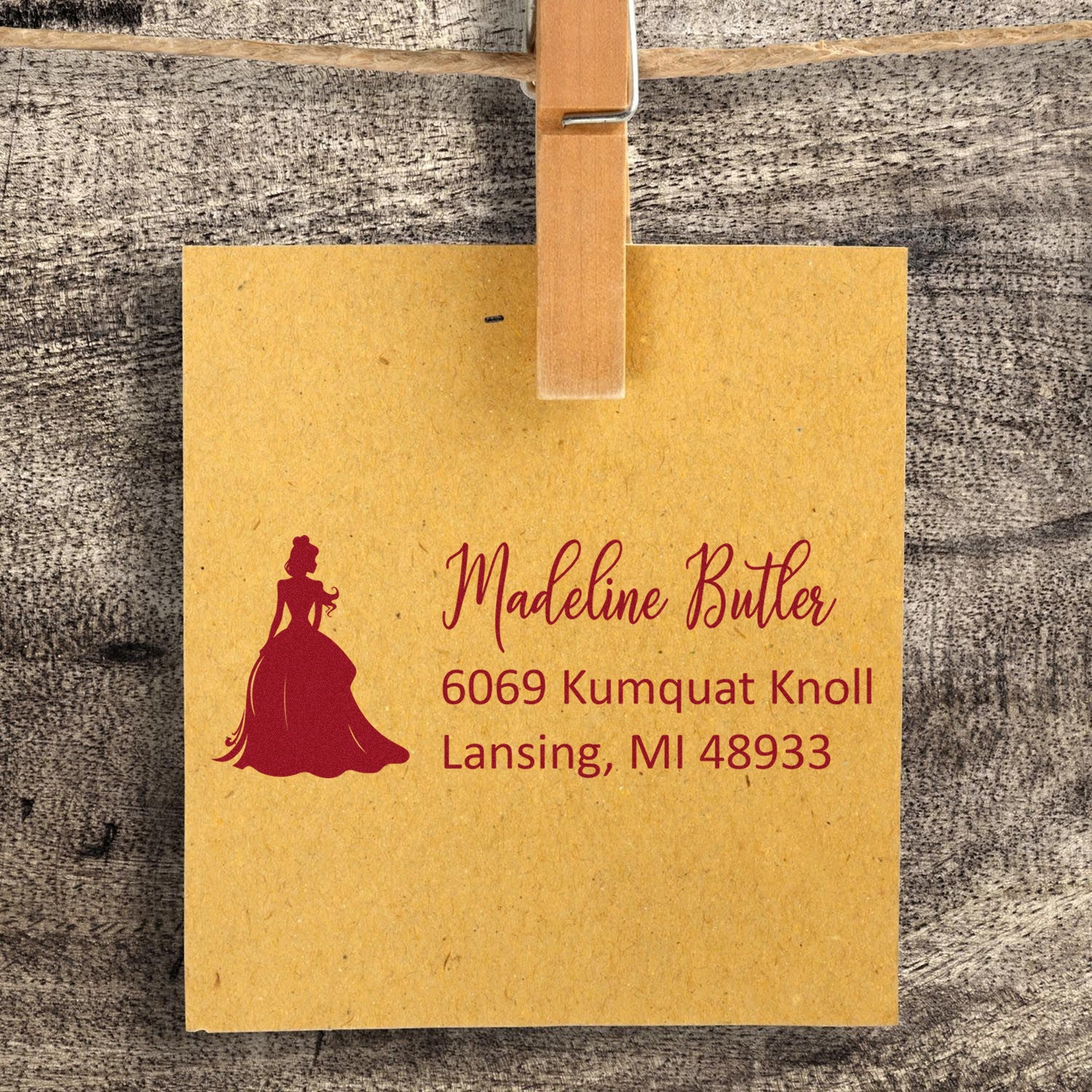 Yellow custom address stamp and seal label with burgundy silhouette, script name, and wooden clothespin on rustic wood.