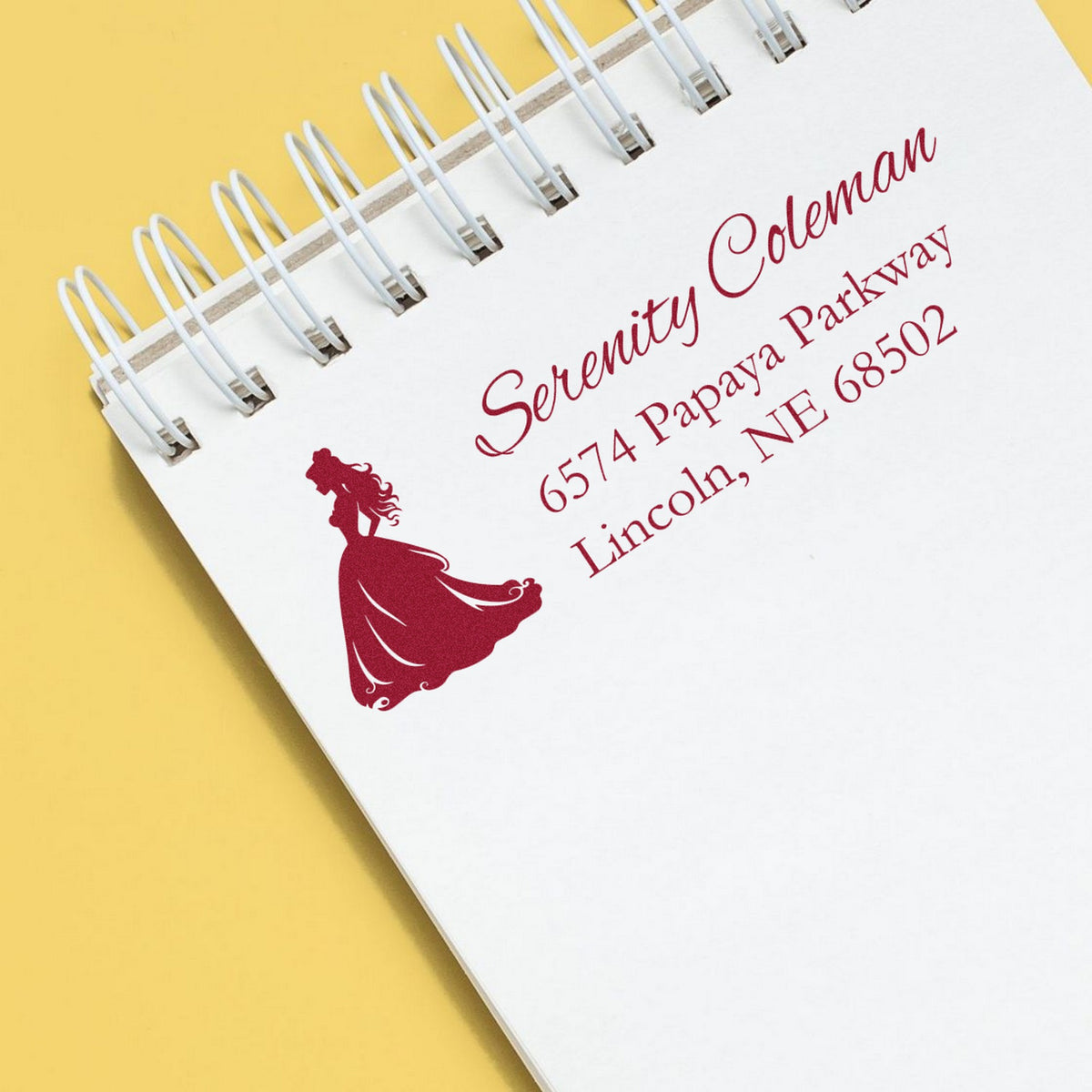 White spiral notebook on yellow background with burgundy custom stamp and seal for Serenity Coleman, featuring a woman silhouette.