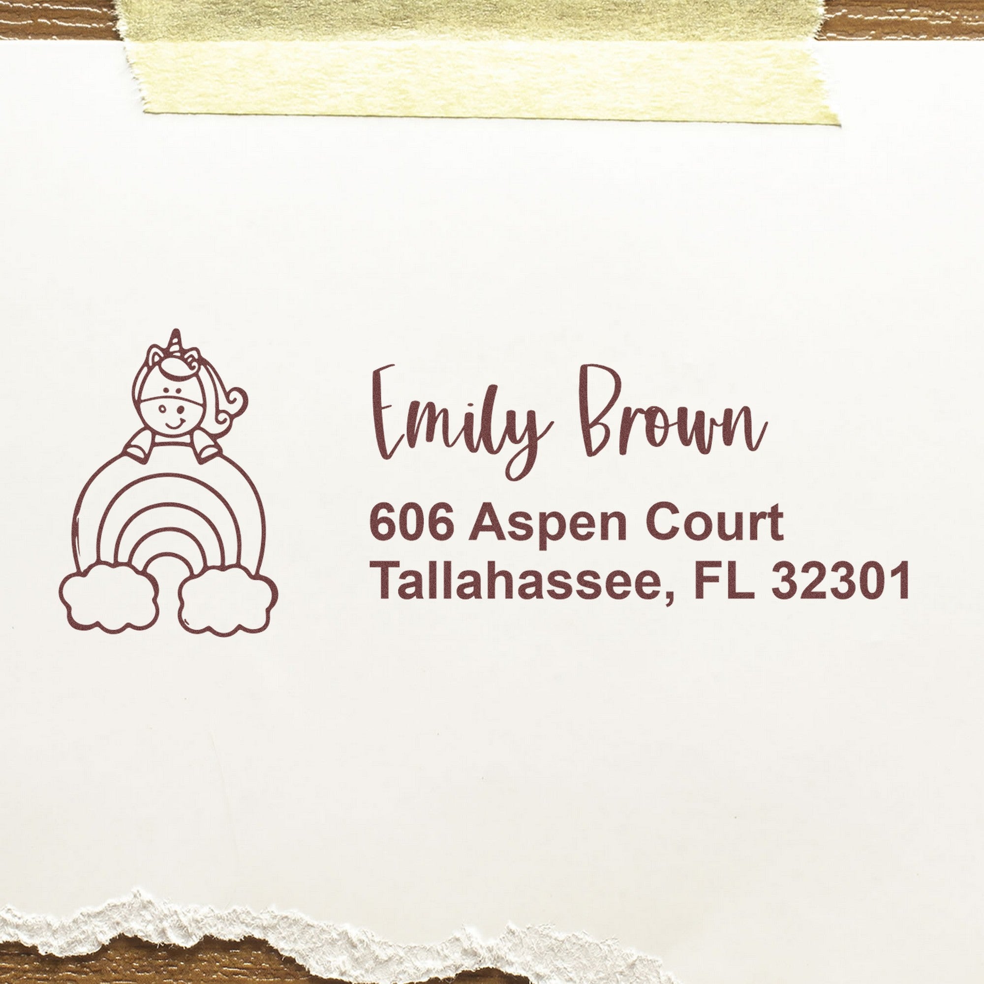 Brown custom address stamp and seal with unicorn on rainbow, Emily Brown, Tallahassee FL, on white paper with taped edges.