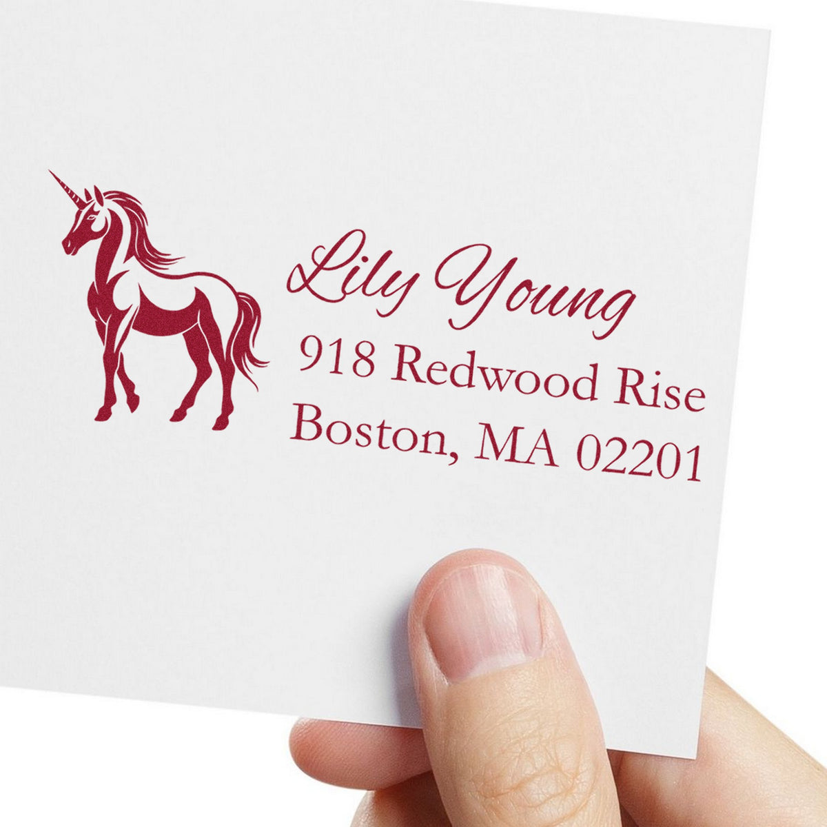 Burgundy custom address stamp with unicorn seal and Lily Young address on white paper, held between fingers.