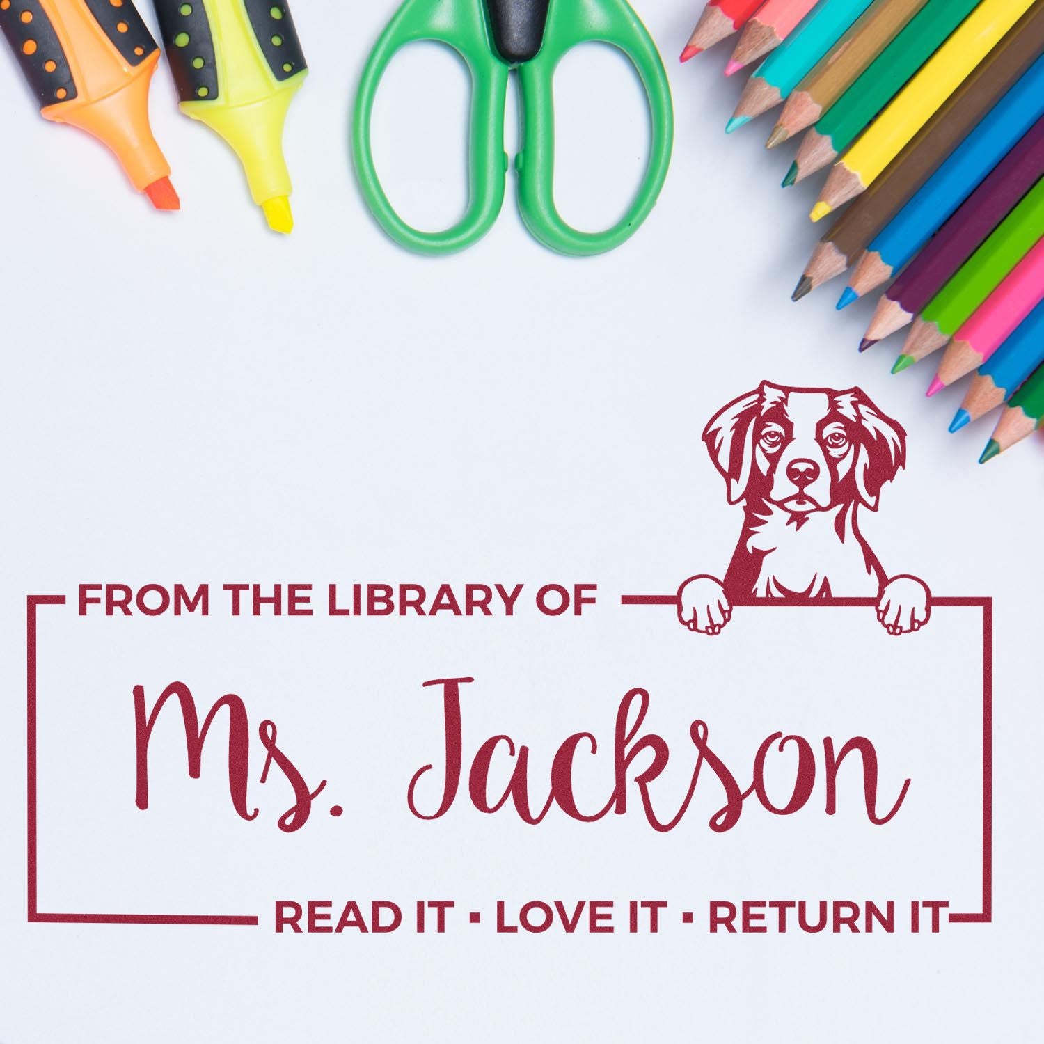 Custom red library stamp seal for Ms. Jackson with dog graphic, framed by colored pencils, green scissors, and markers.