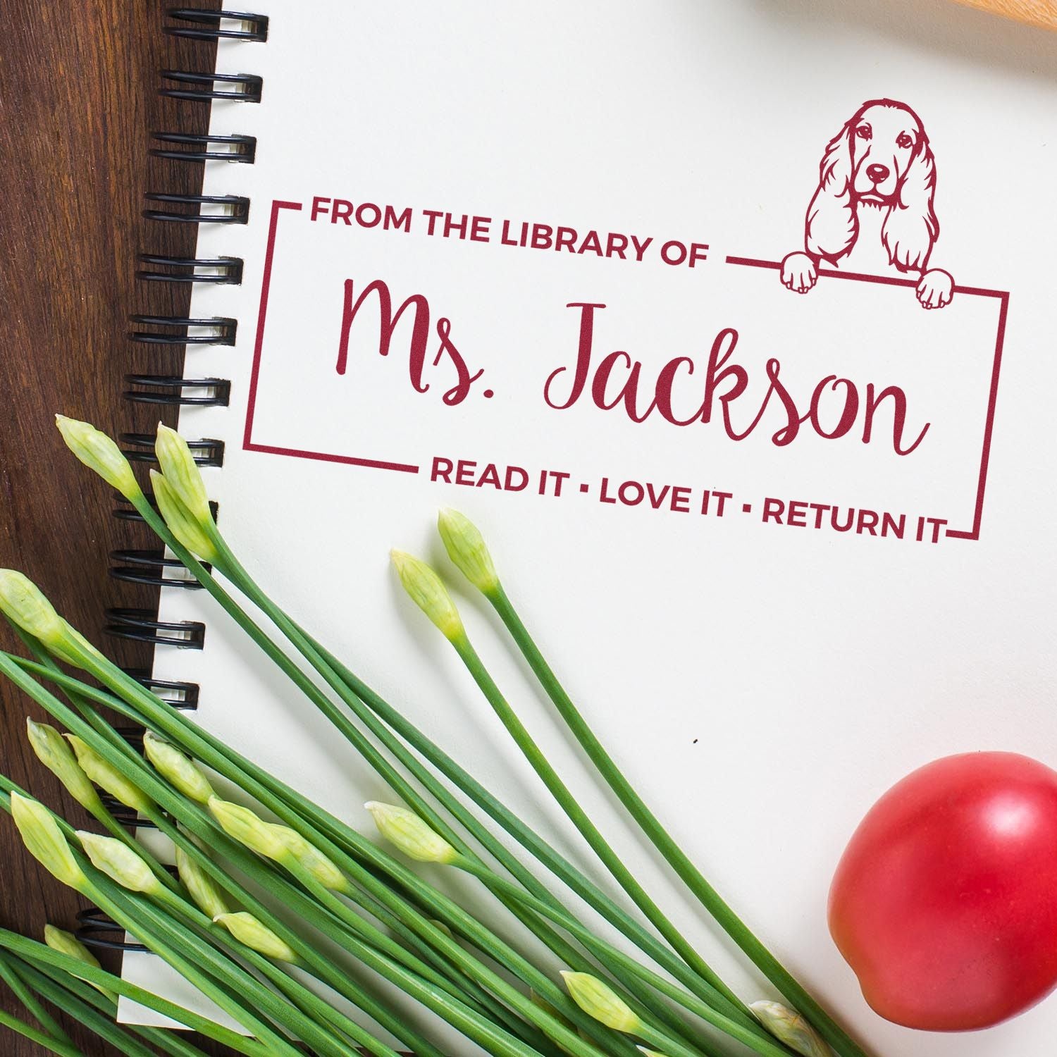 Maroon custom library stamp and seal with dog, From the Library of Ms. Jackson, on a white spiral notebook.