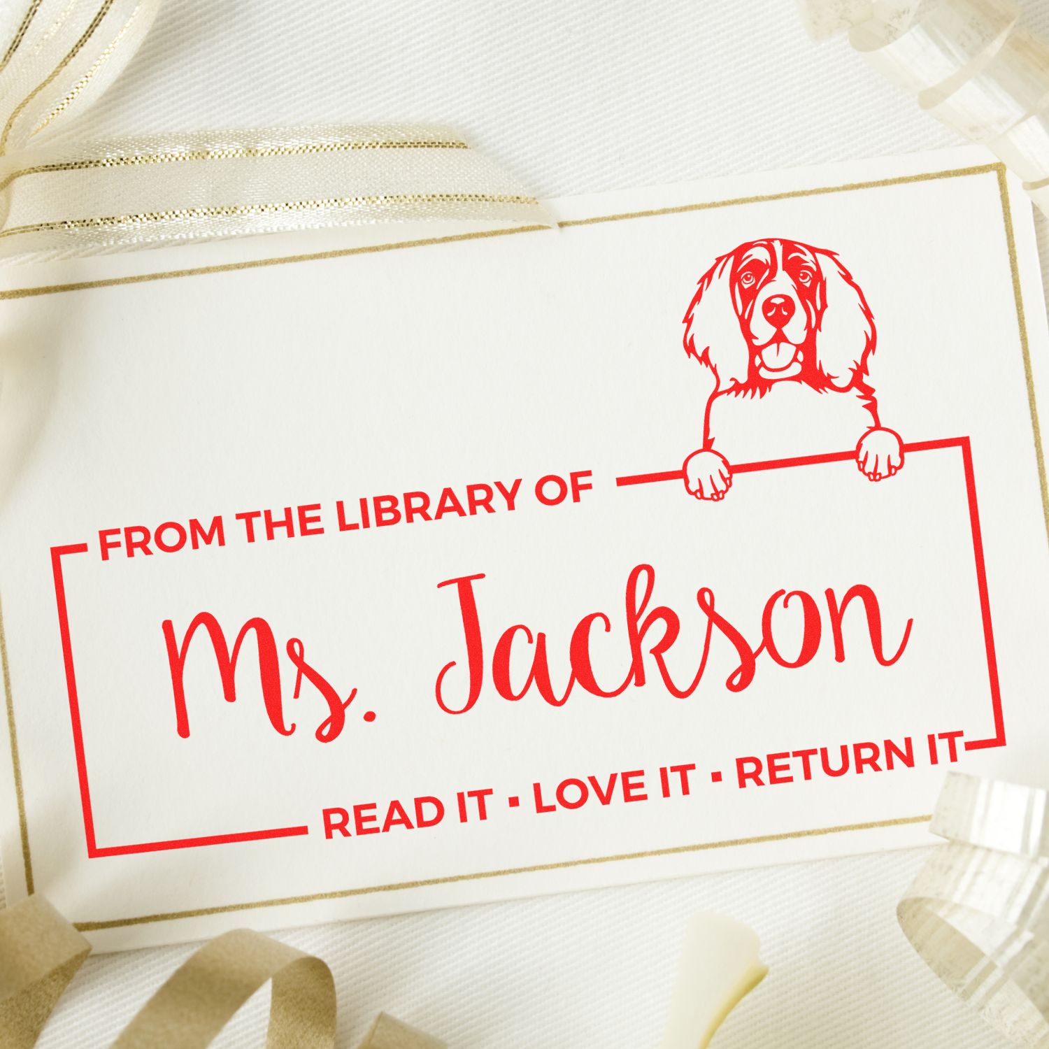 Red custom library stamp seal for Ms. Jackson with dog illustration on cream paper and gold border.