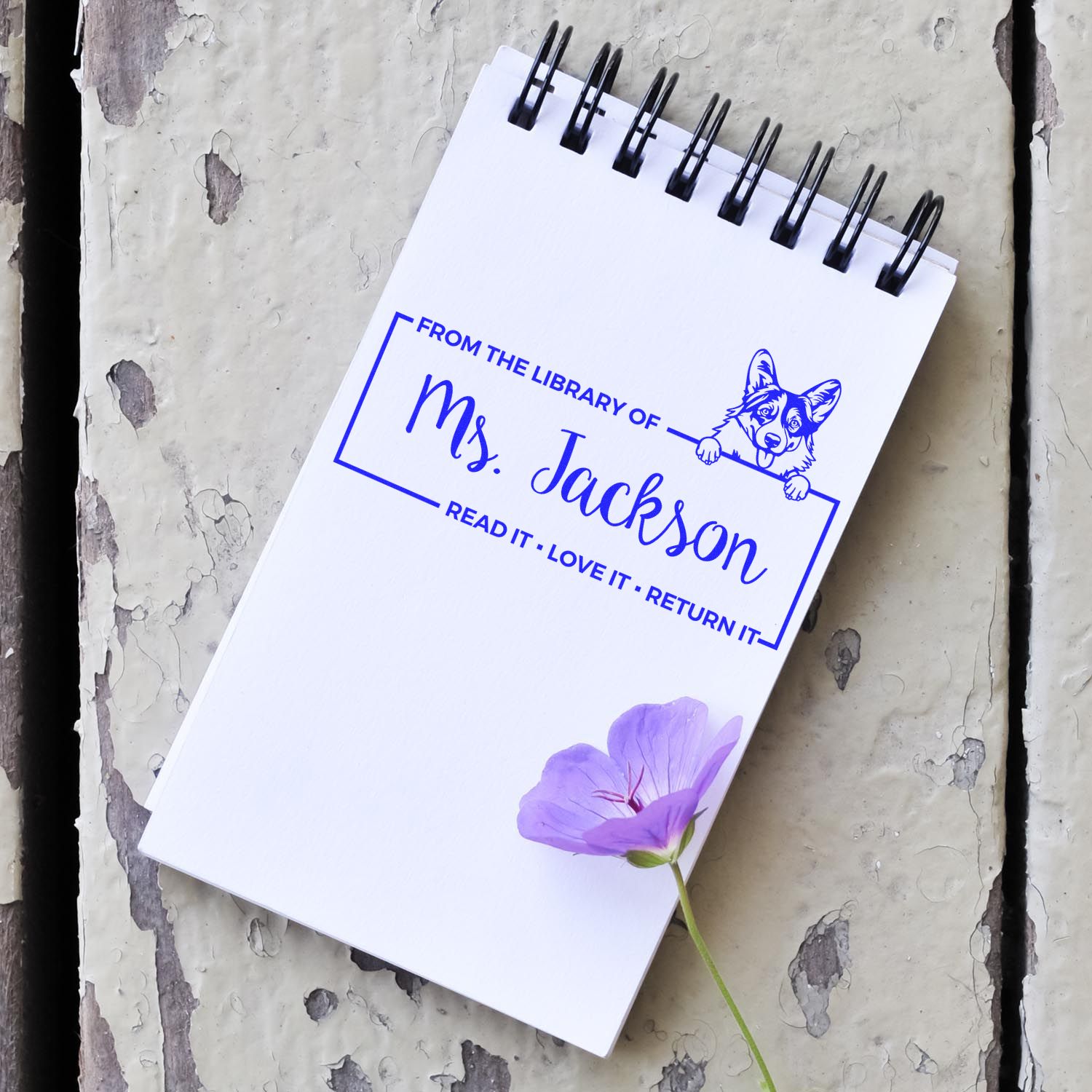 White spiral notebook with blue custom library stamp and seal for Ms. Jackson, featuring a corgi and purple flower.