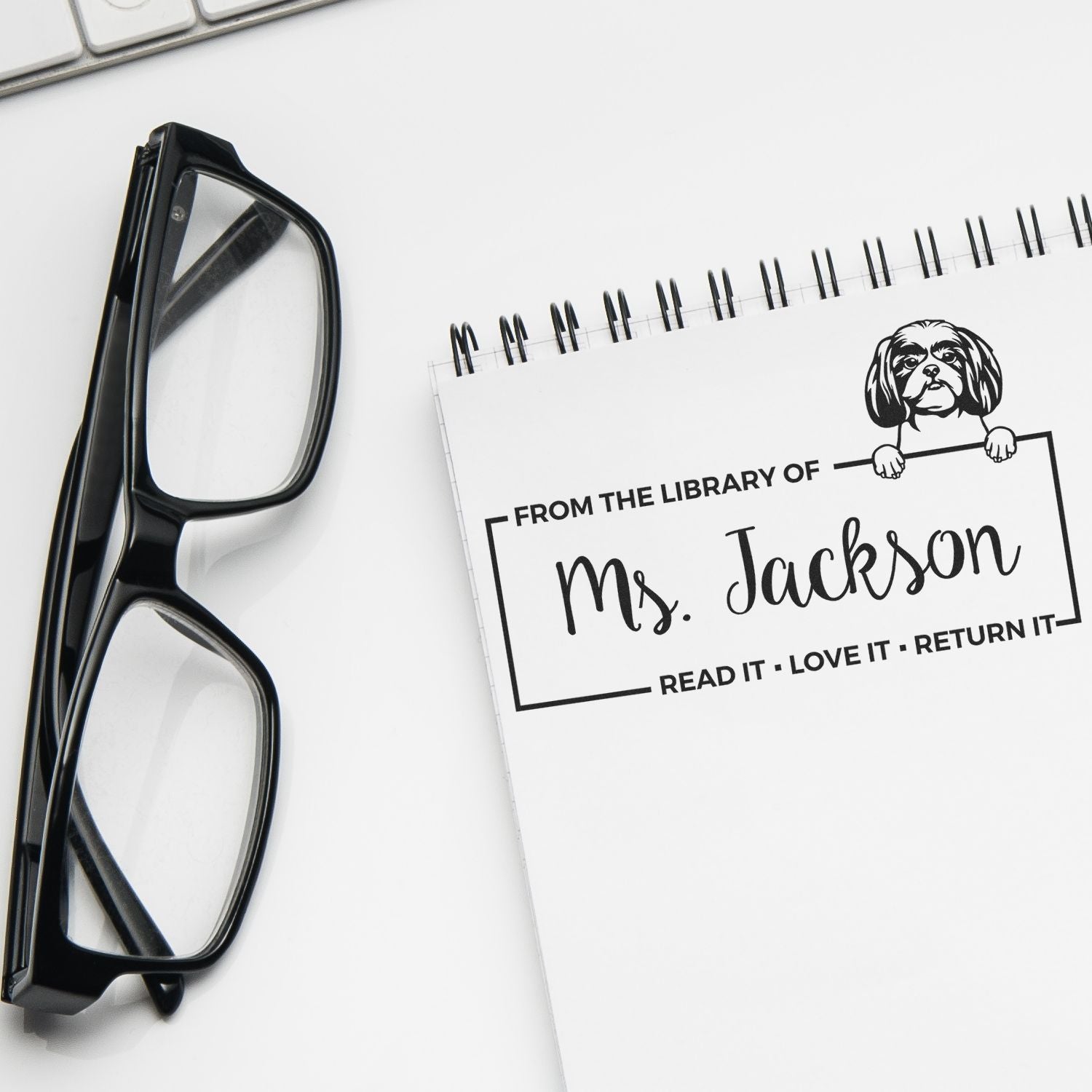 Black eyeglasses beside a white notebook with a custom library stamp and seal reading From the Library of Ms. Jackson.