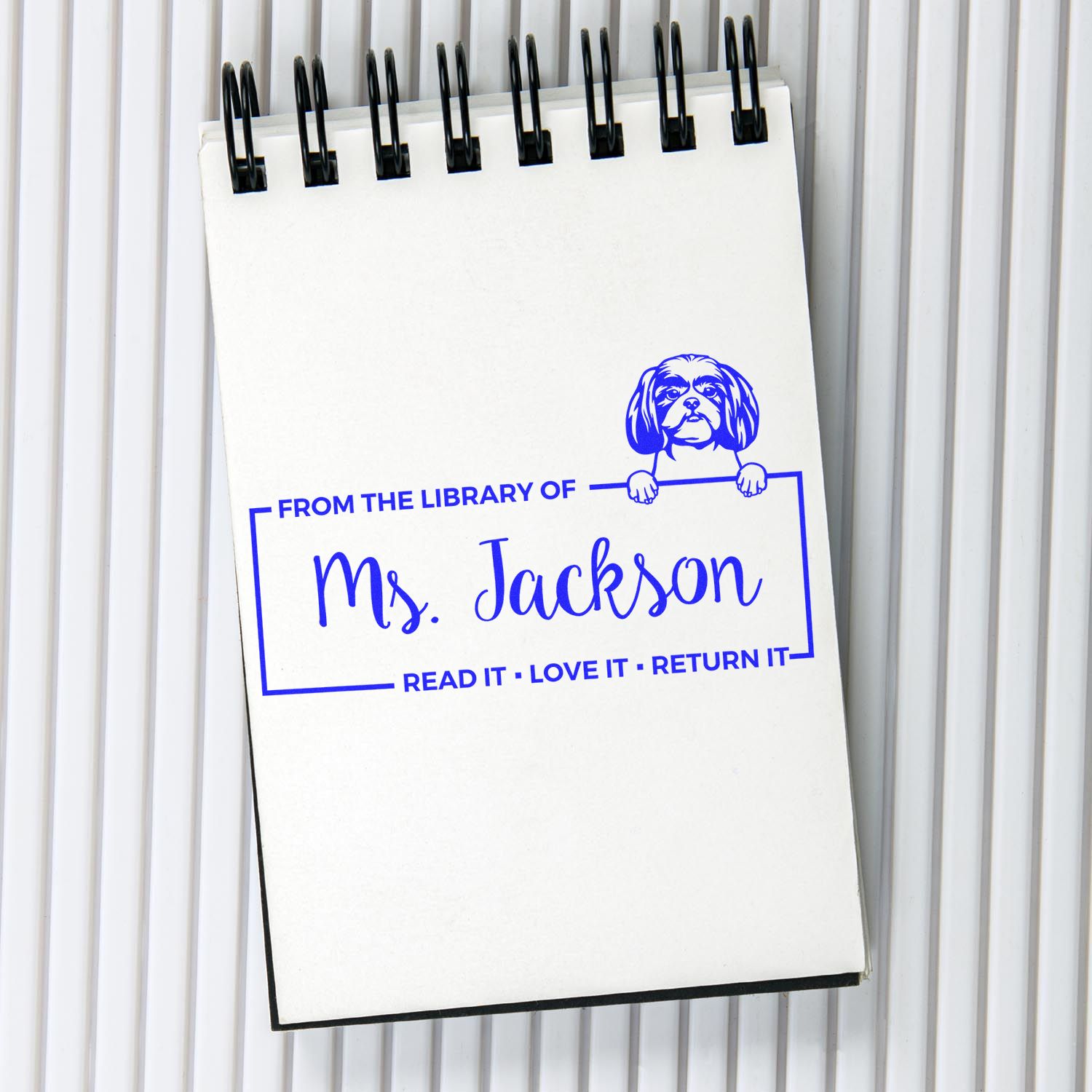 Blue custom library stamp seal on white spiral notepad, with dog graphic and Ms. Jackson text.
