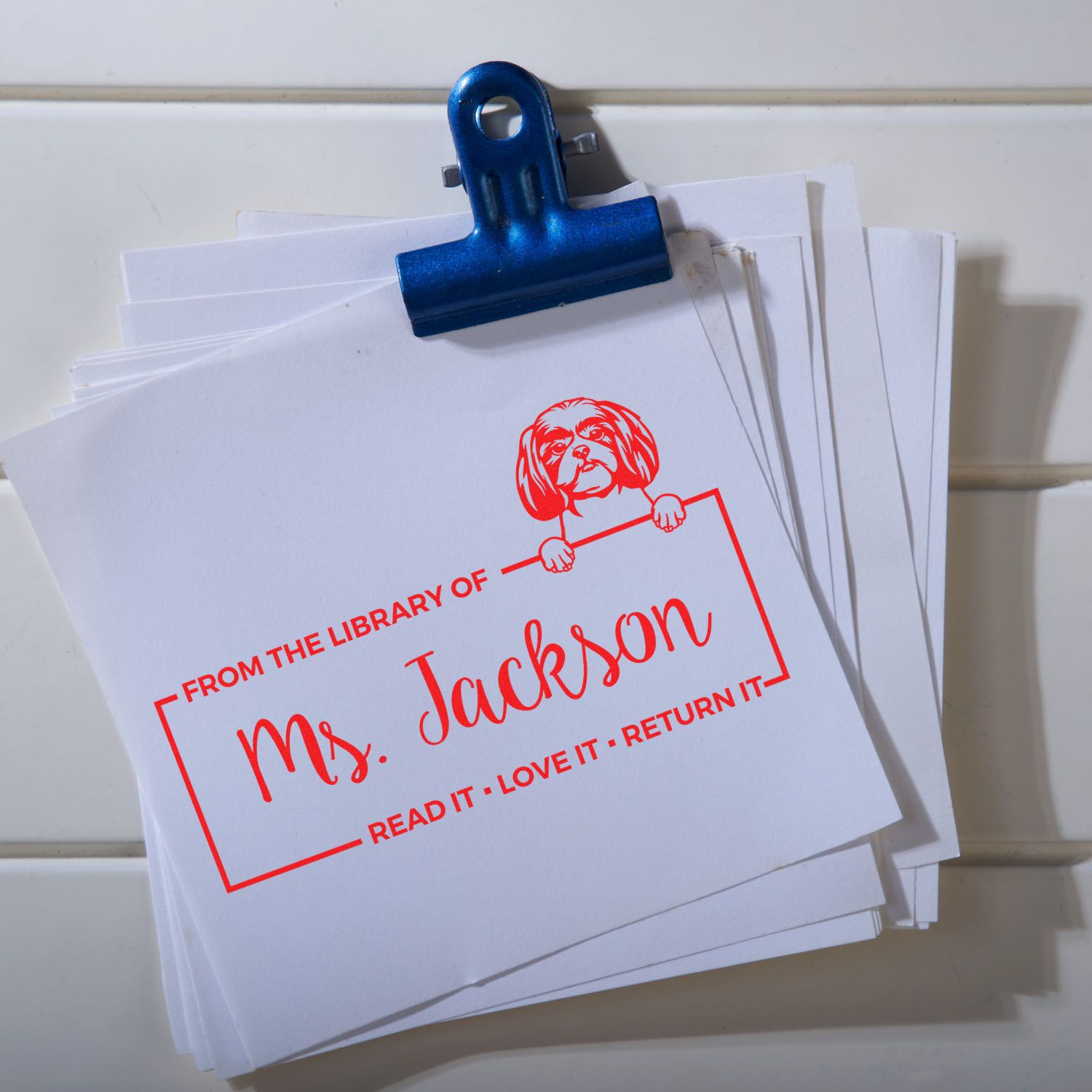 Blue binder clip holding white cards stamped in red with a custom library return-it seal for Ms. Jackson.