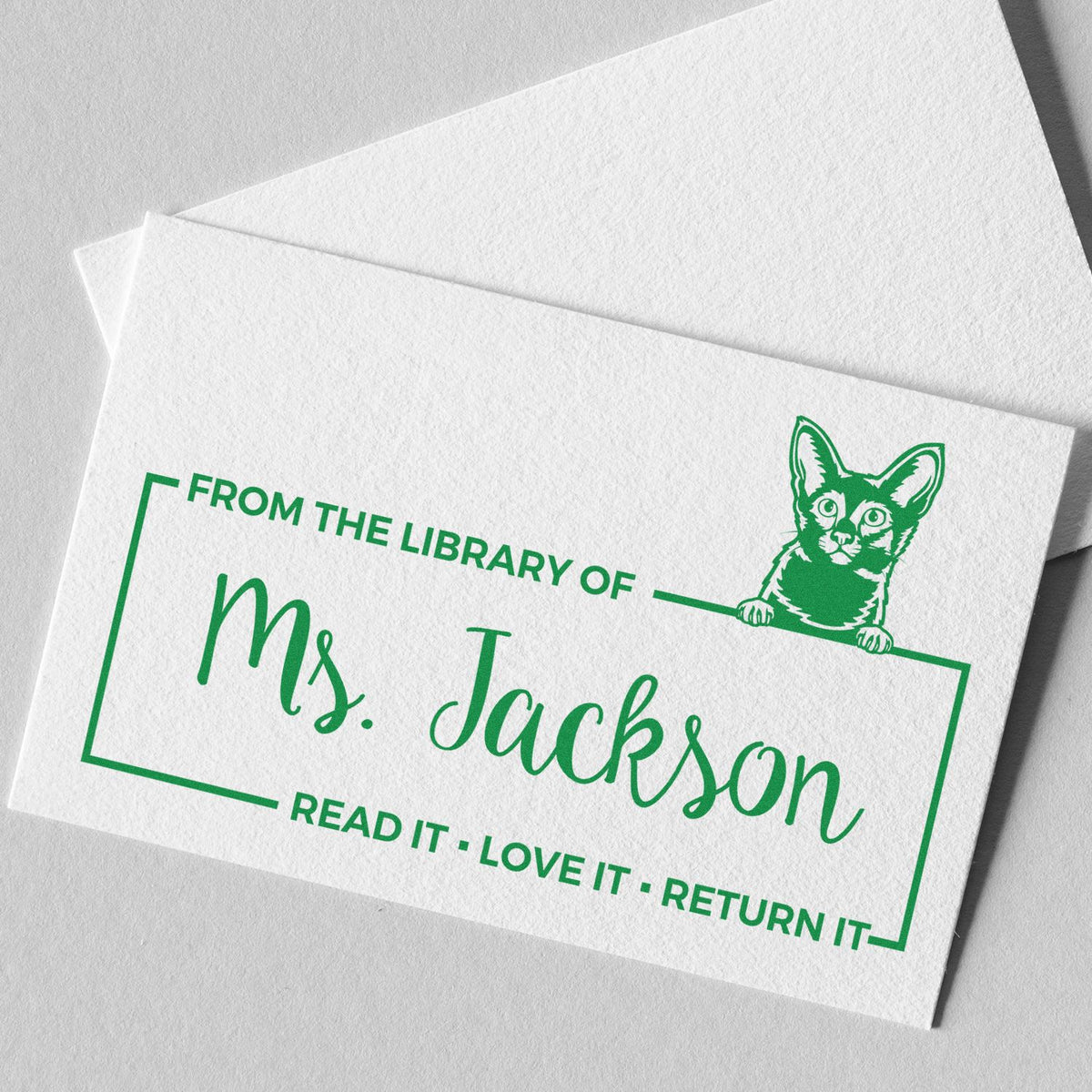 Green custom library stamp with cat seal and Ms. Jackson text on white paper, reading Read it Love it Return it.