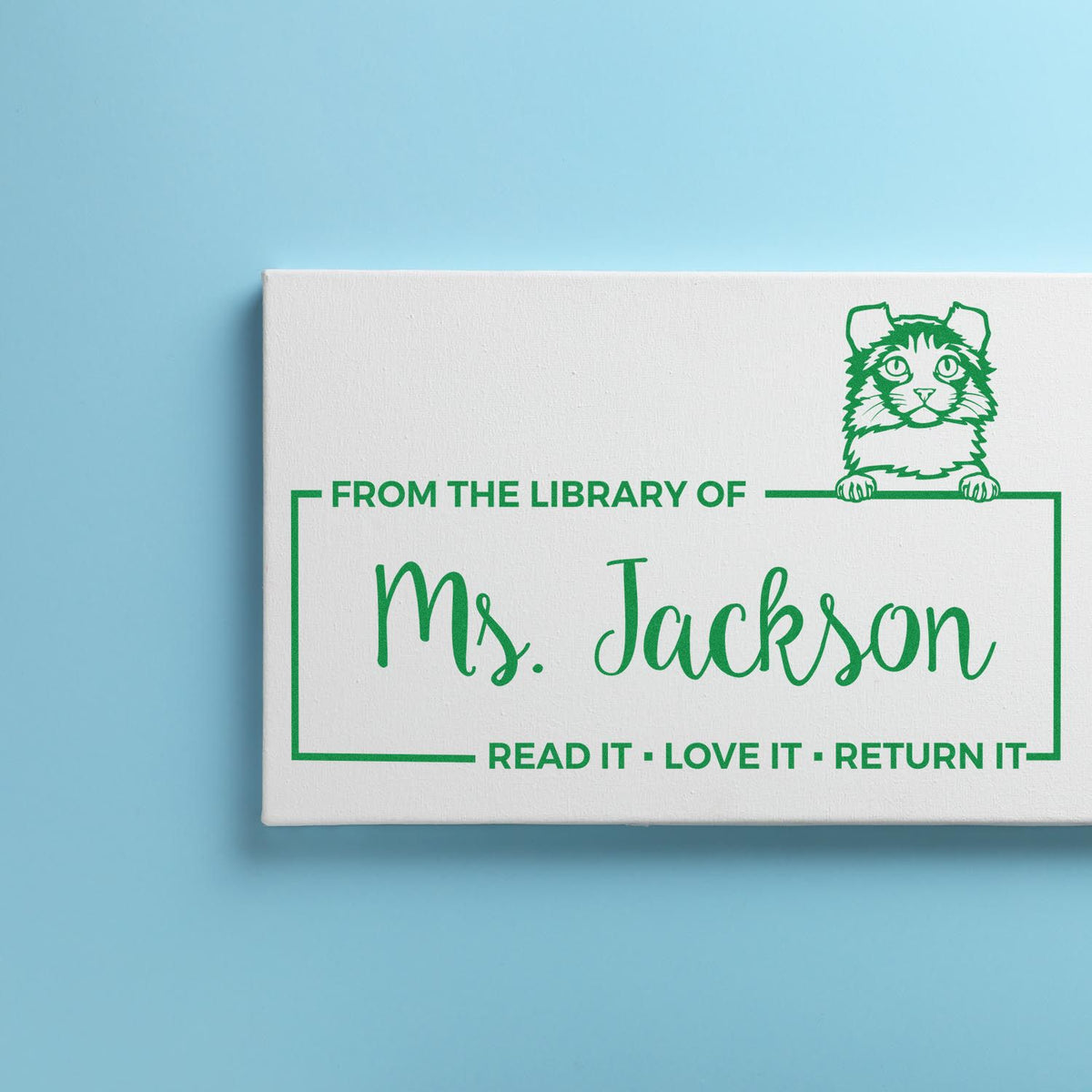 White custom self-inking library stamp with green cat seal, Ms. Jackson text, on a light blue background.