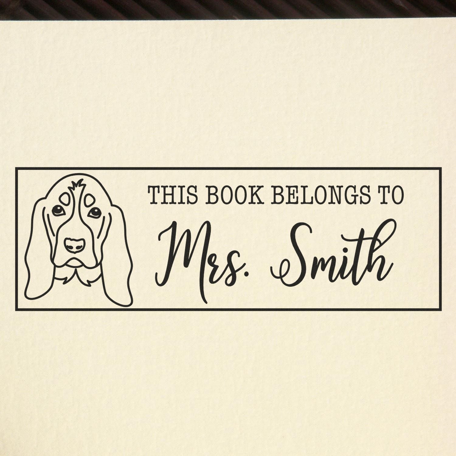 Black custom book stamp with dog outline and This Book Belongs to Mrs. Smith on cream background.