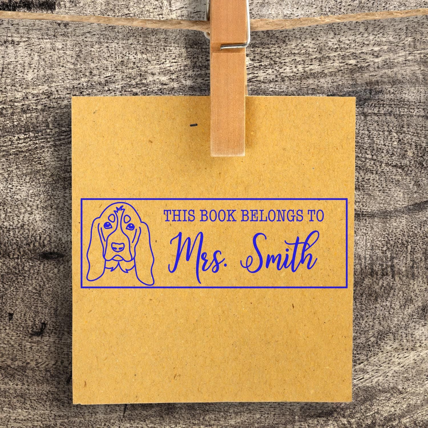 Yellow personalized book stamp and seal with blue dog design and This Book Belongs to Mrs. Smith on rustic wood.