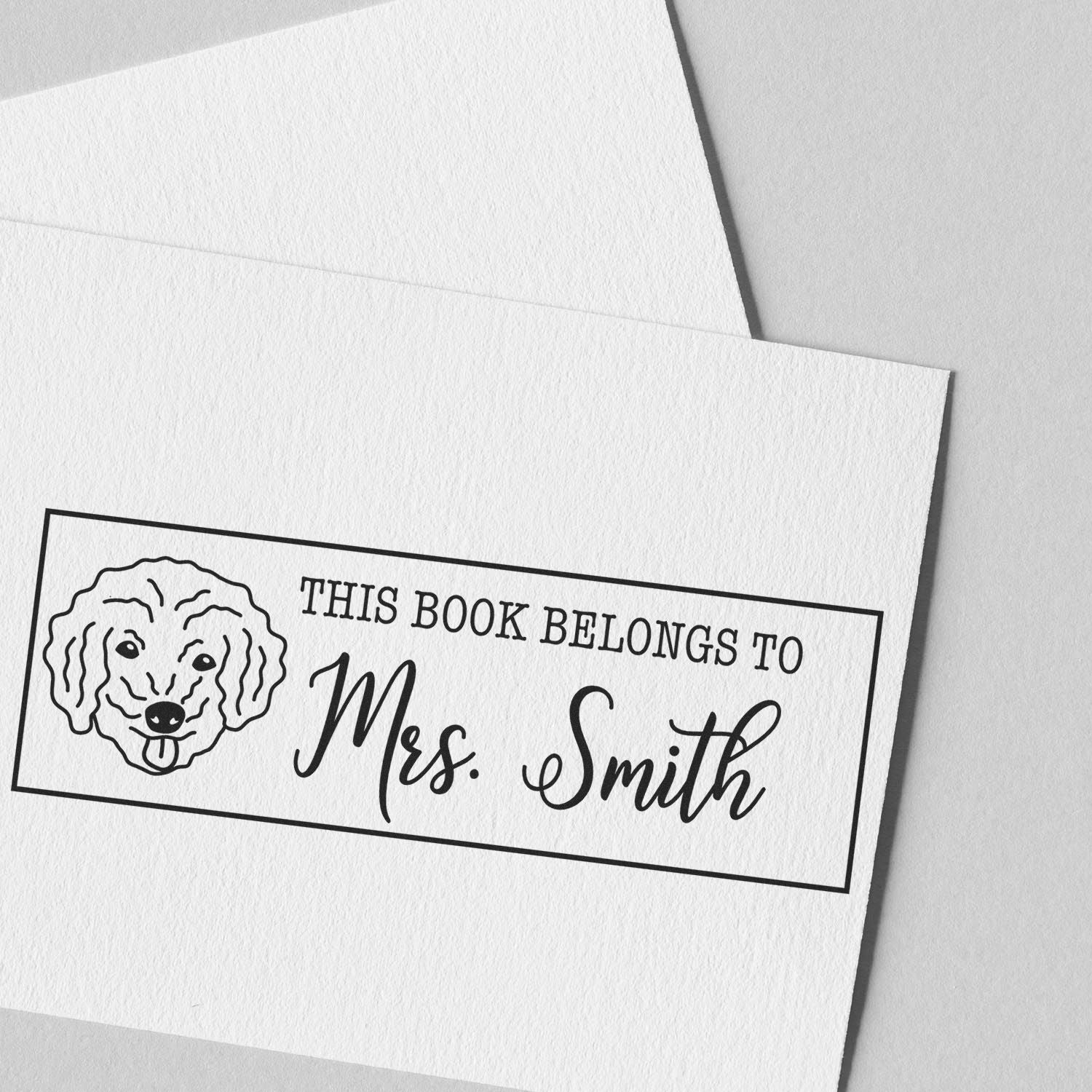 Black custom book stamp with dog seal and This Book Belongs to Mrs. Smith on white textured paper.